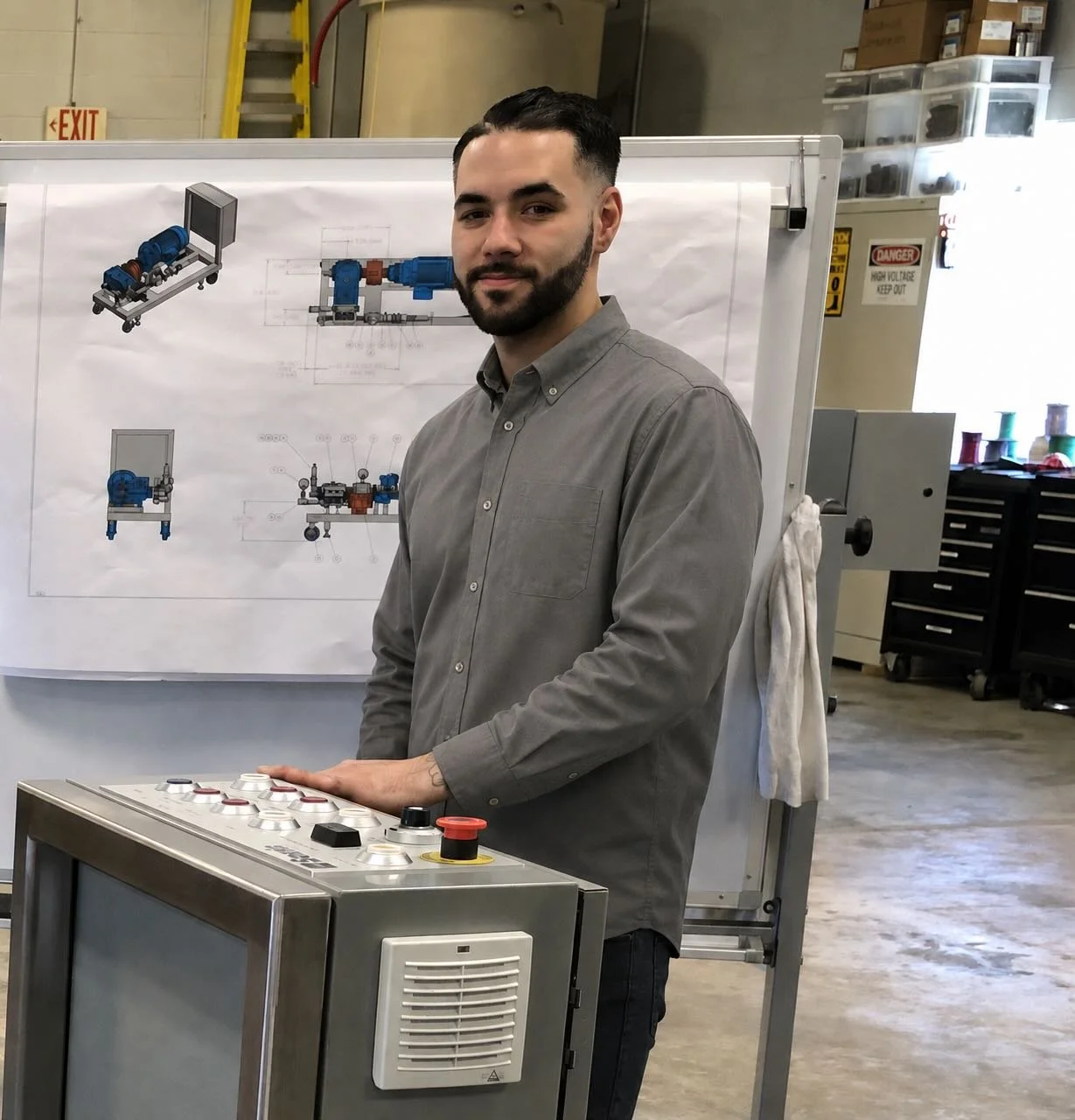 A man standing in front of a technical drawing of a mechanical device in an industrial workshop, with his hand on a control panel.