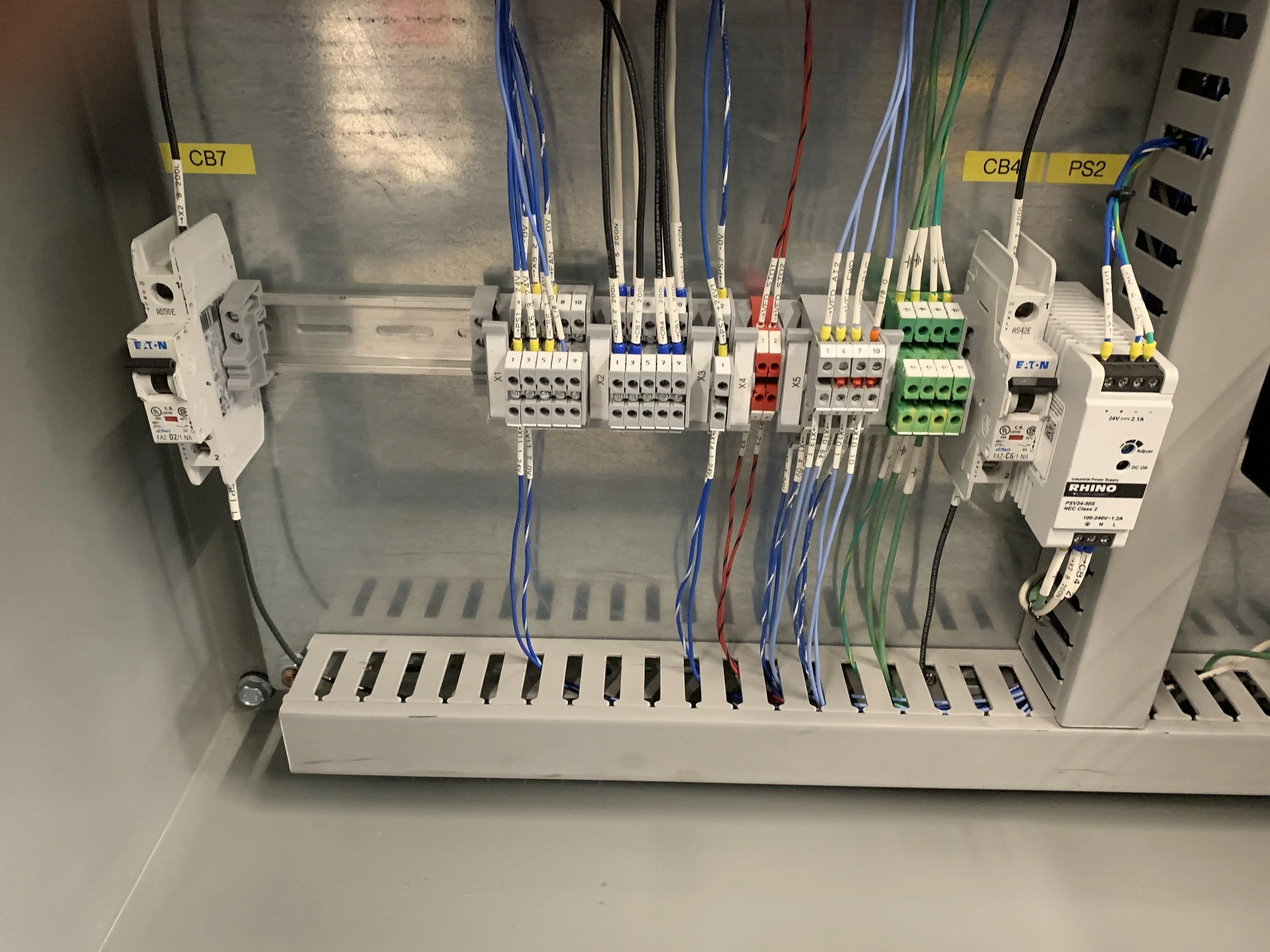 An electrical control panel inside a metal enclosure, containing various color-coded wires connected to terminal blocks and circuit breakers.