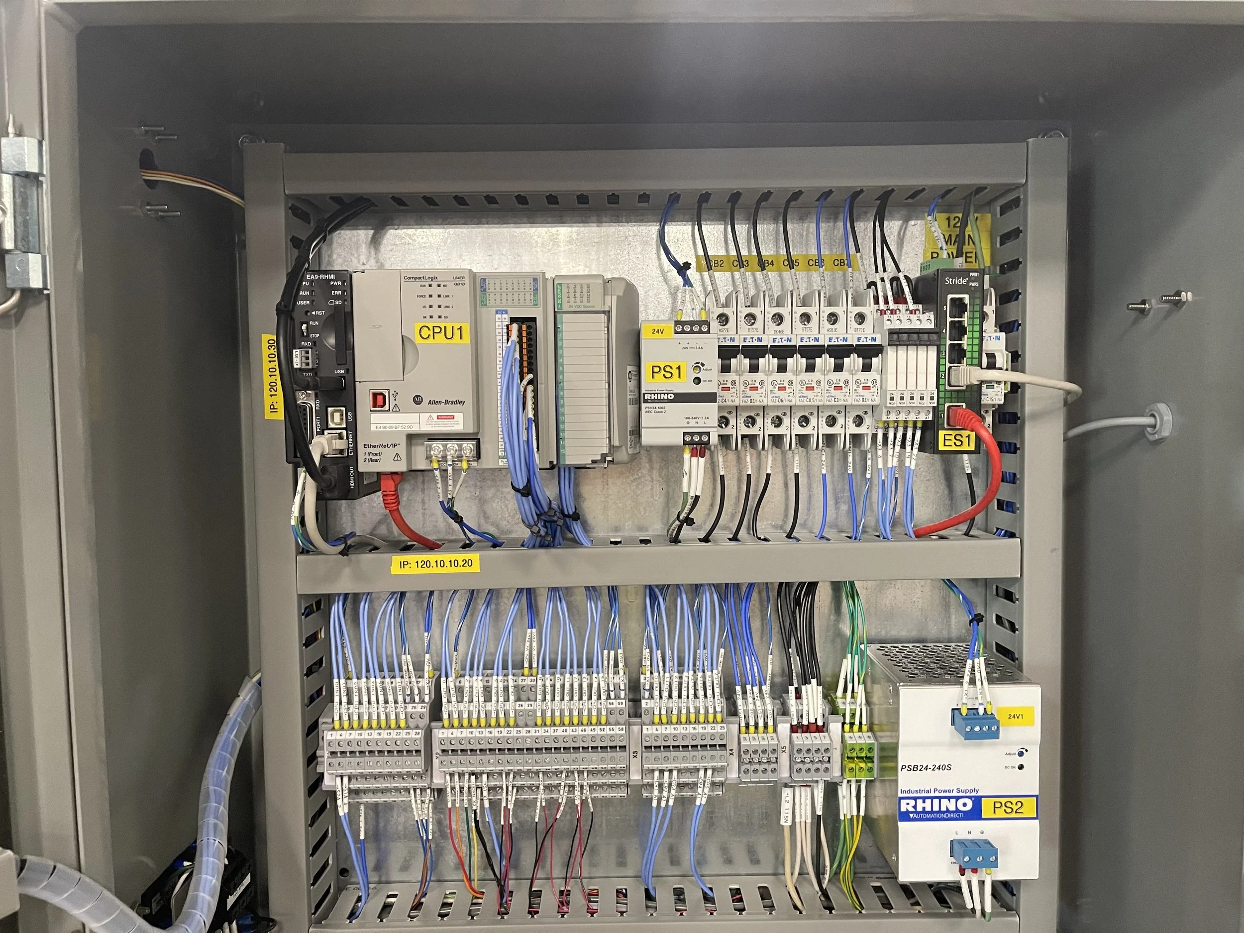 Electrical control panel with various wires, switches, and modules labeled with yellow tags, including CPU, power supply, and terminal blocks.