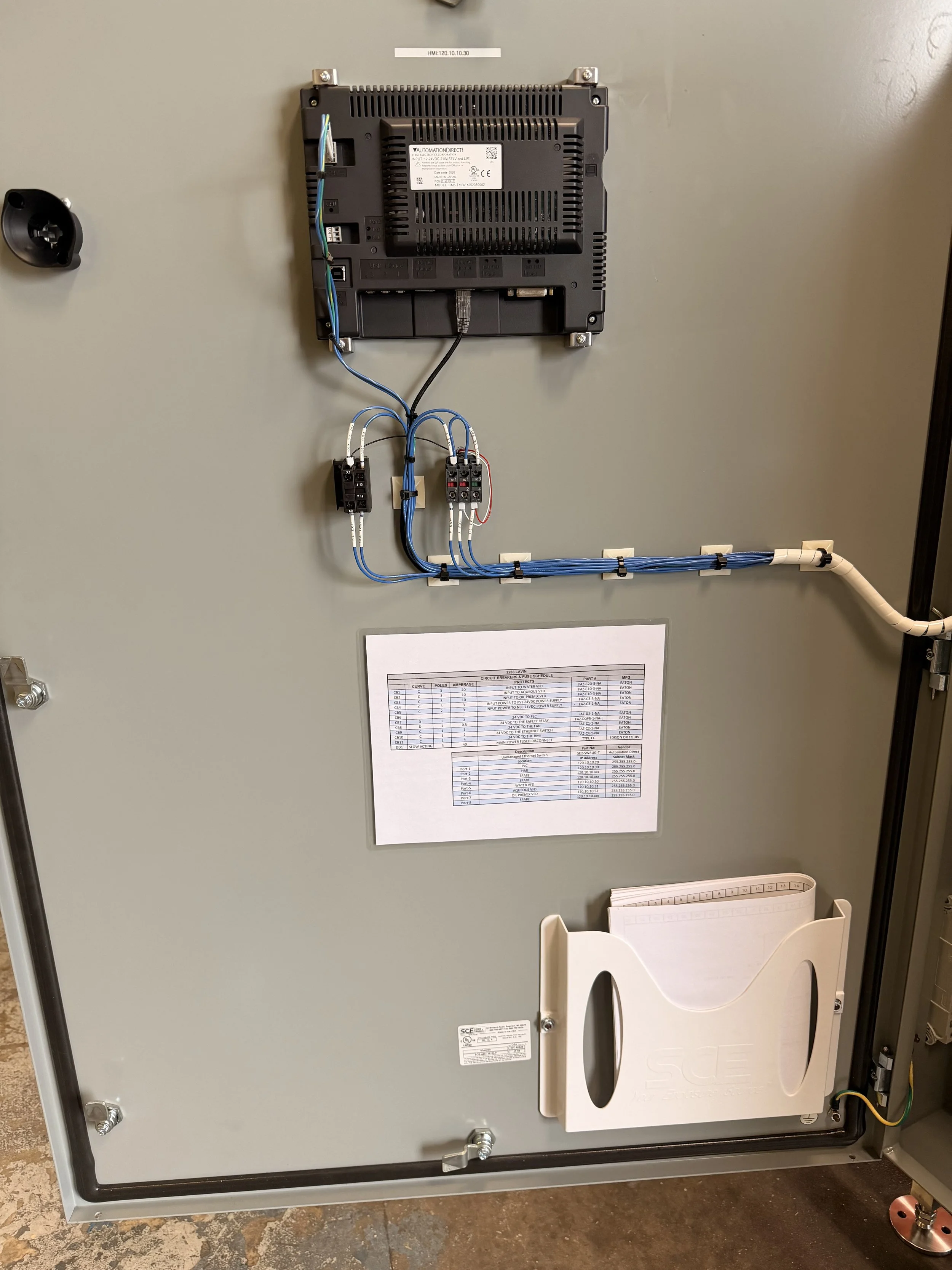 Electrical panel with wiring, a white protective cover, and a printed circuit diagram on the door.