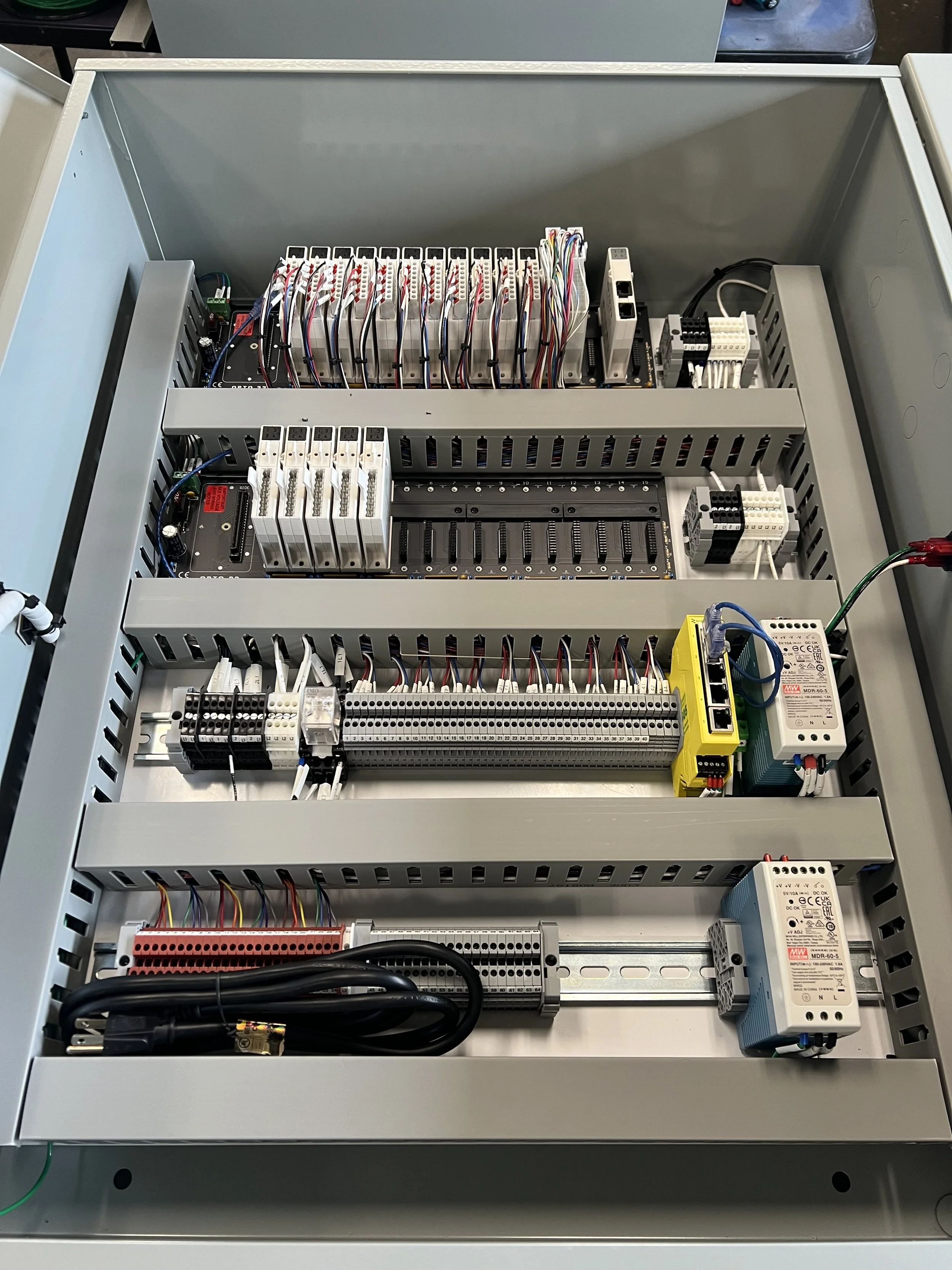 Open electrical control panel with various wiring, circuit breakers, and electronic components inside a gray metal enclosure.