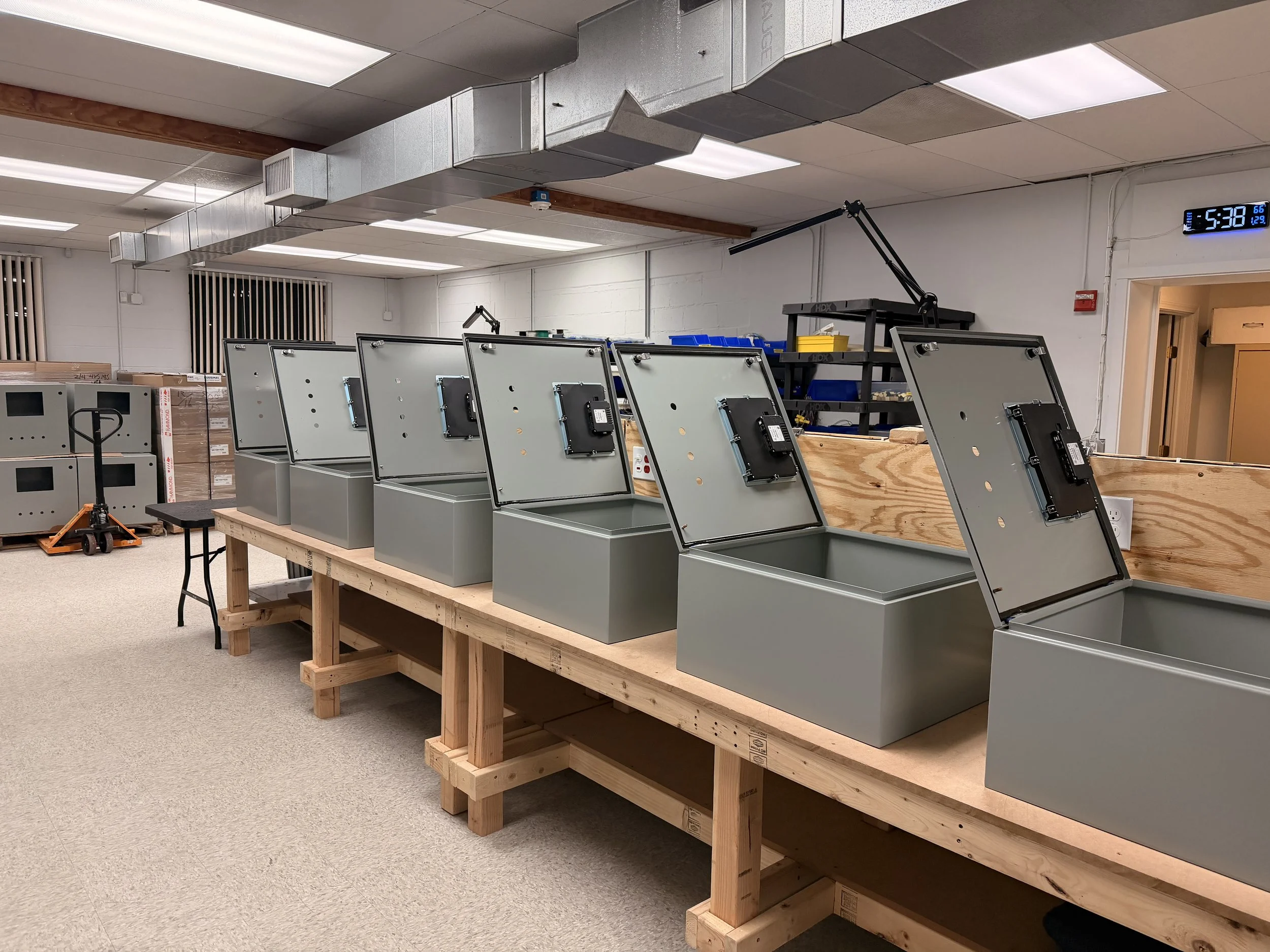 Row of electronic devices with open back panels on a wooden workbench in a workshop.