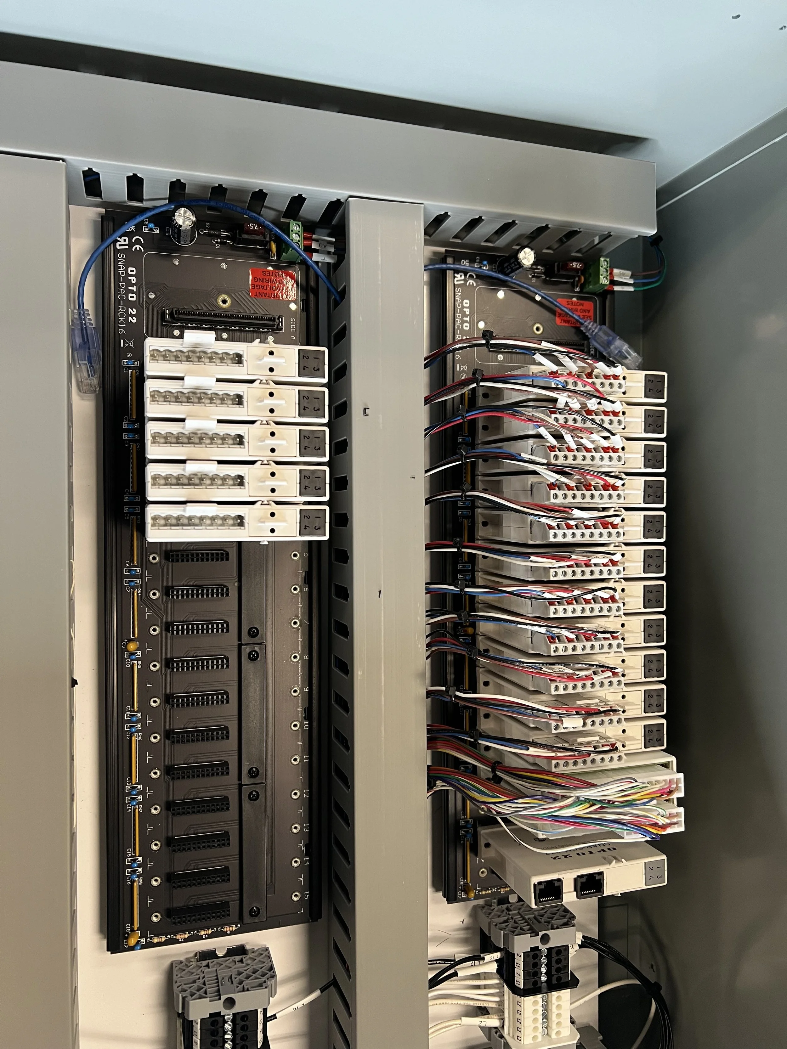 Close-up of an electrical control panel with multiple terminal blocks, wiring, and electronic components mounted on a wall.