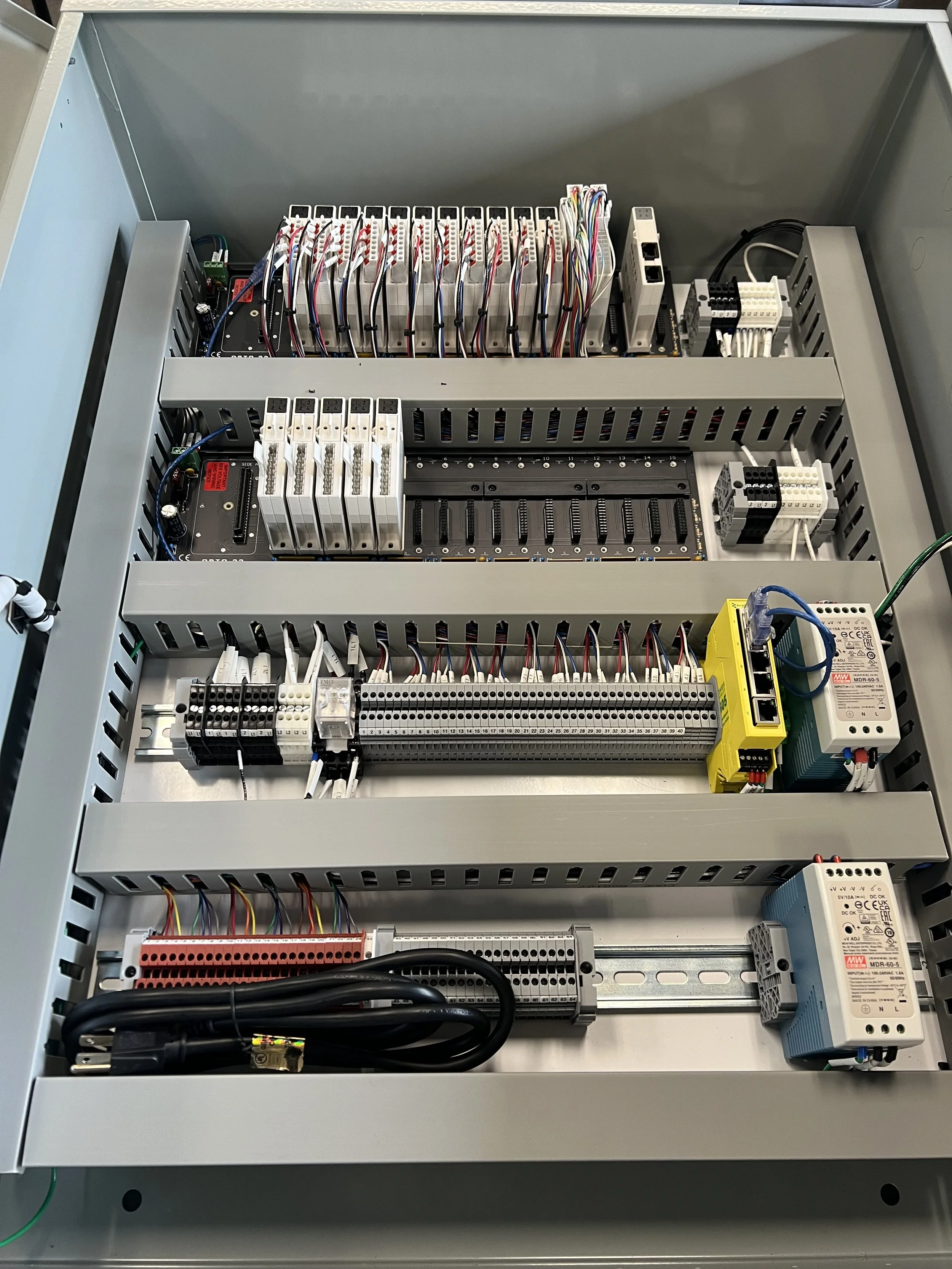 Open electrical control panel with interconnected wires, circuit boards, relays, and wiring terminal blocks.