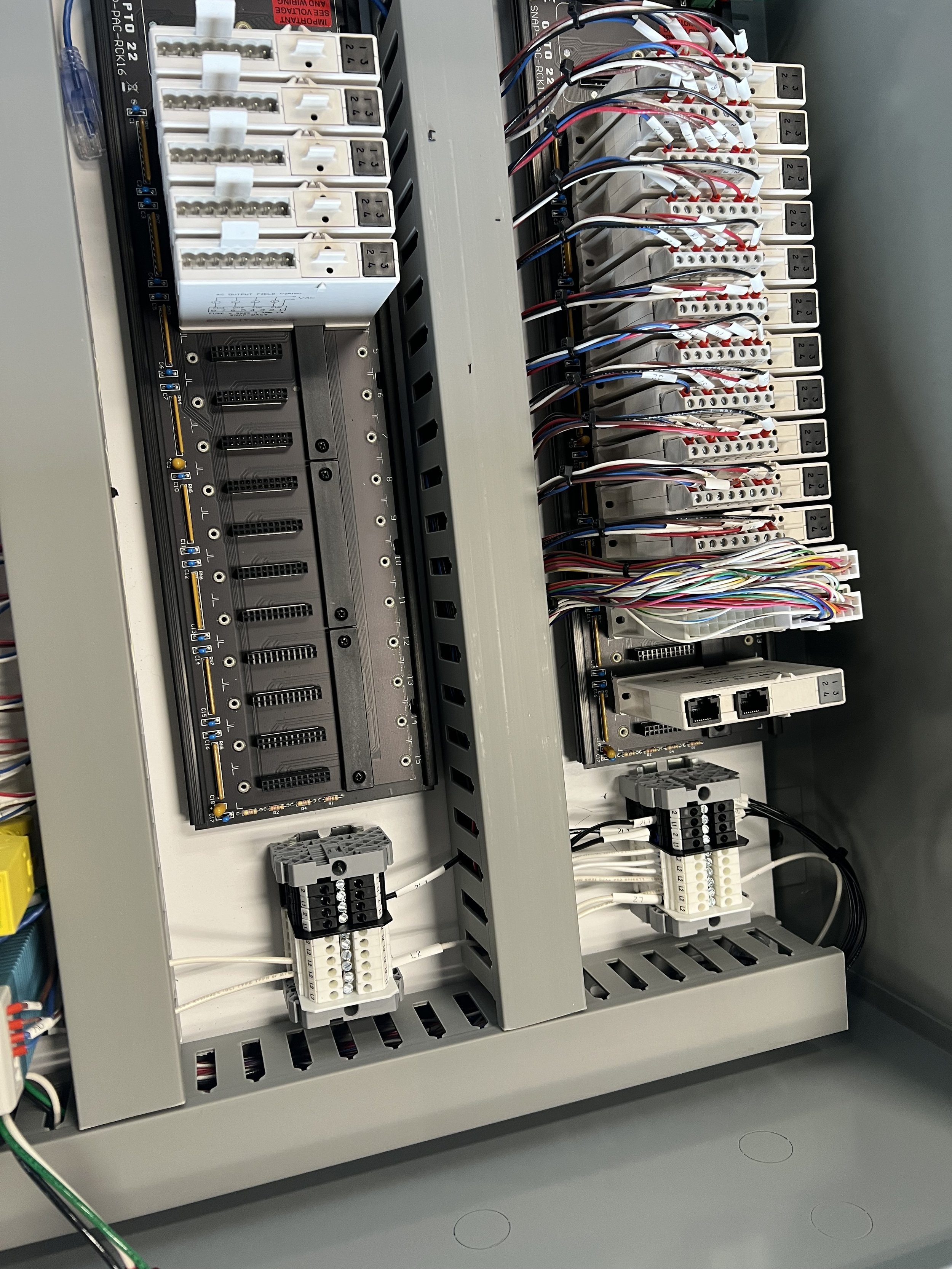 An electrical control panel with wiring, relays, terminal blocks, and circuit breakers arranged inside a metal enclosure.