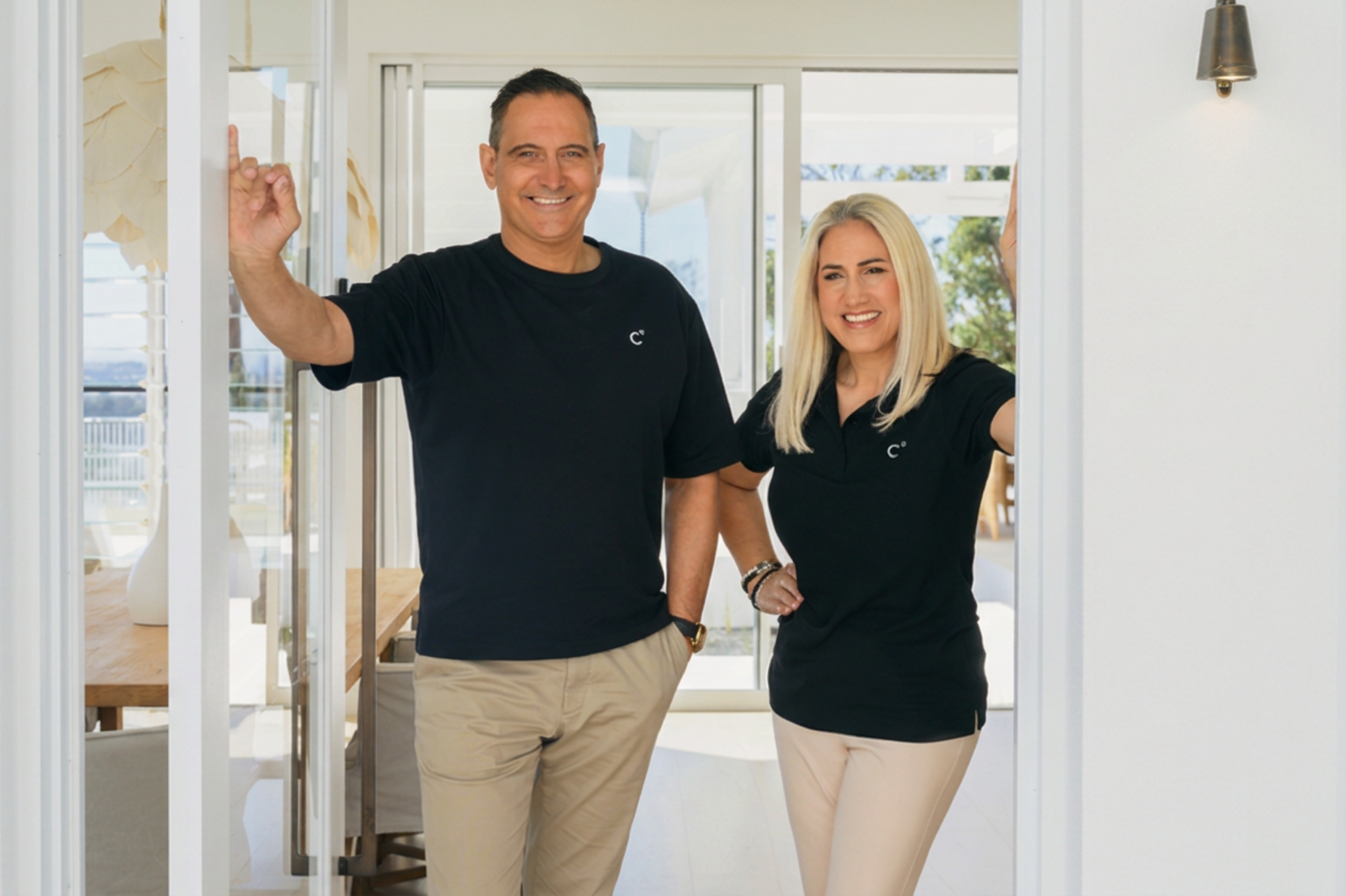 Roberto and Lisa standing in the doorway of a contemporary home, with Roberto making an OK gesture.