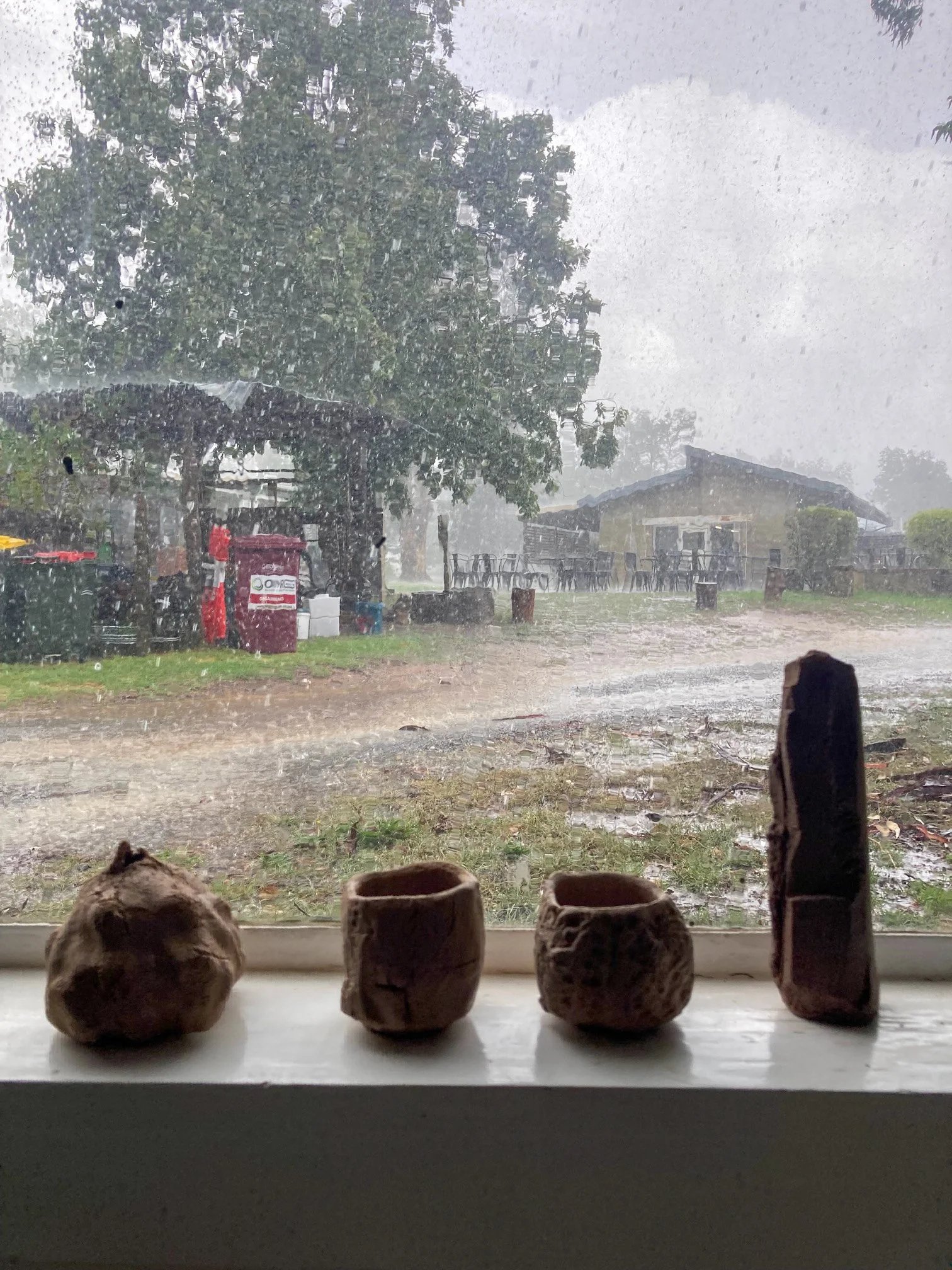 Four ceramic vessels of various sizes on a window sill with rain in the background. 