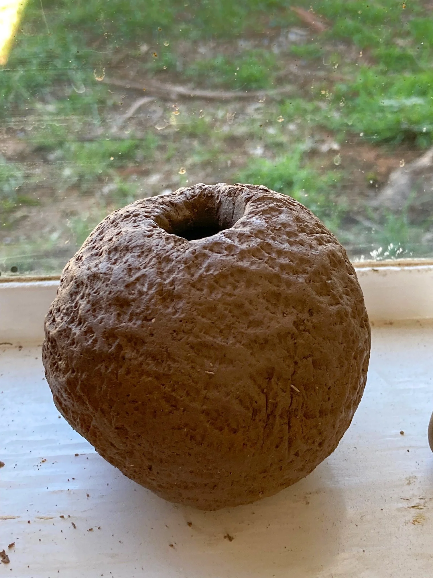 Brown spherical ceramic vessel on a window still with a rough texture. 