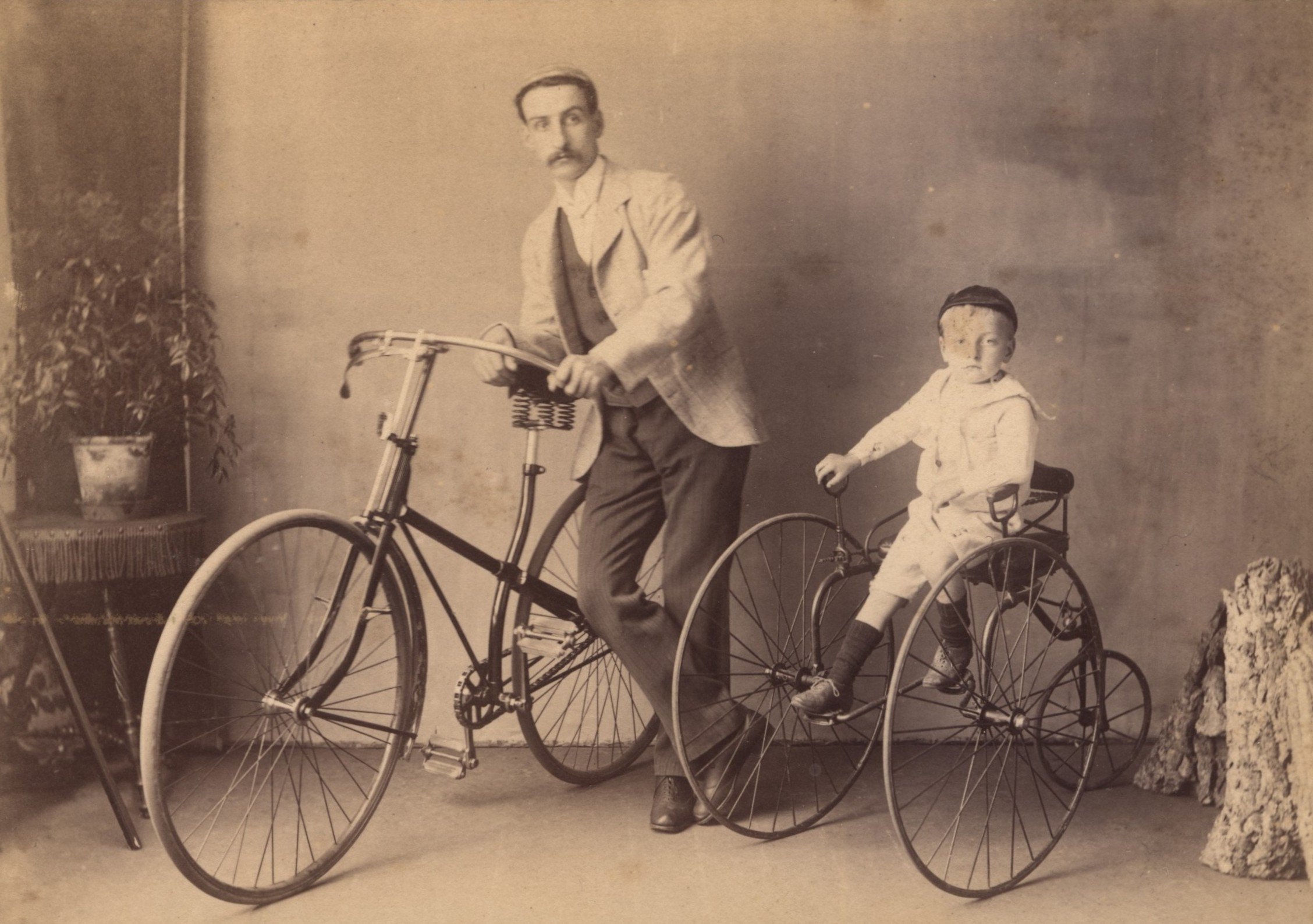 Man with cross frame safety bicycle  and child with early tricycle