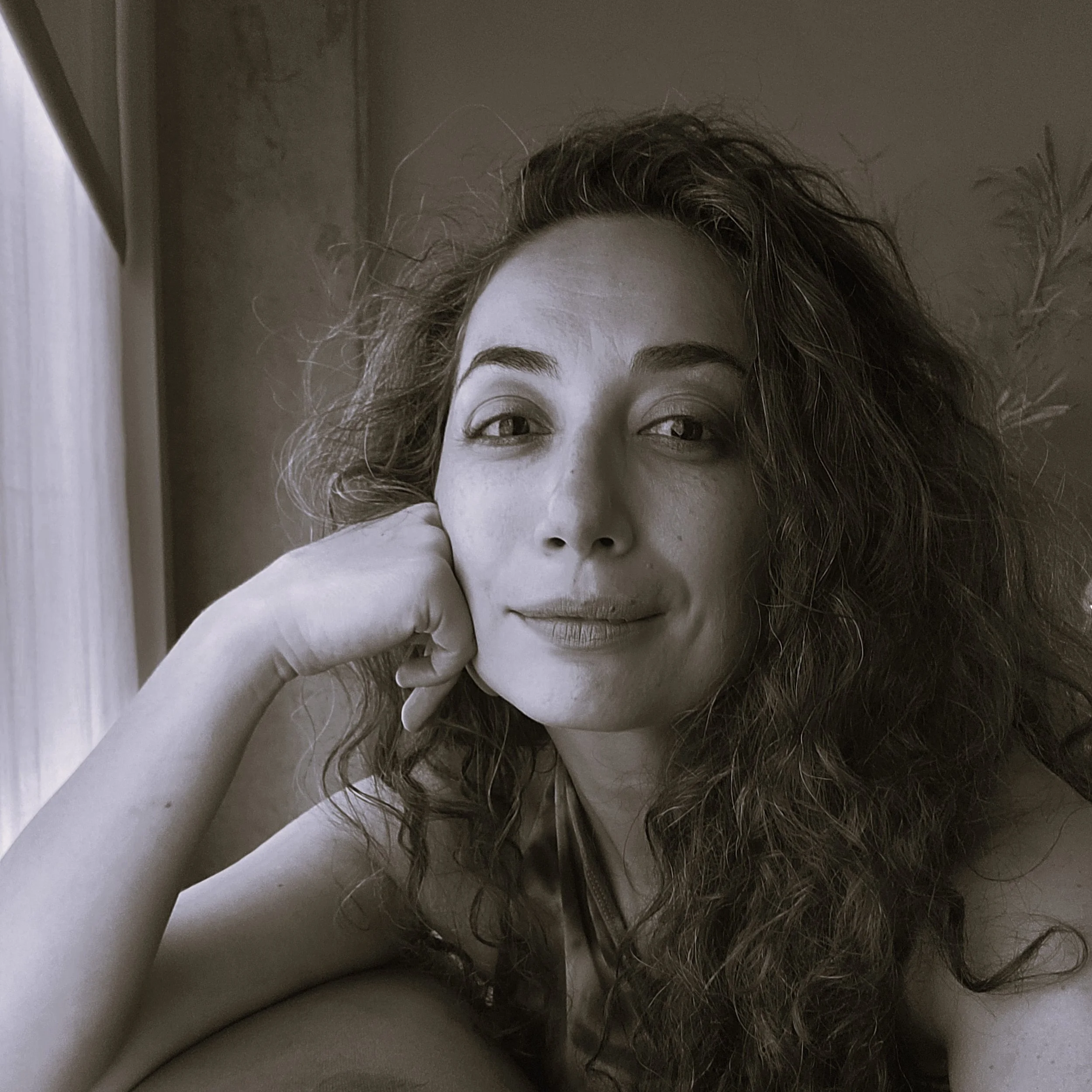 A woman with curly hair resting her chin on her hand and looking at the camera.