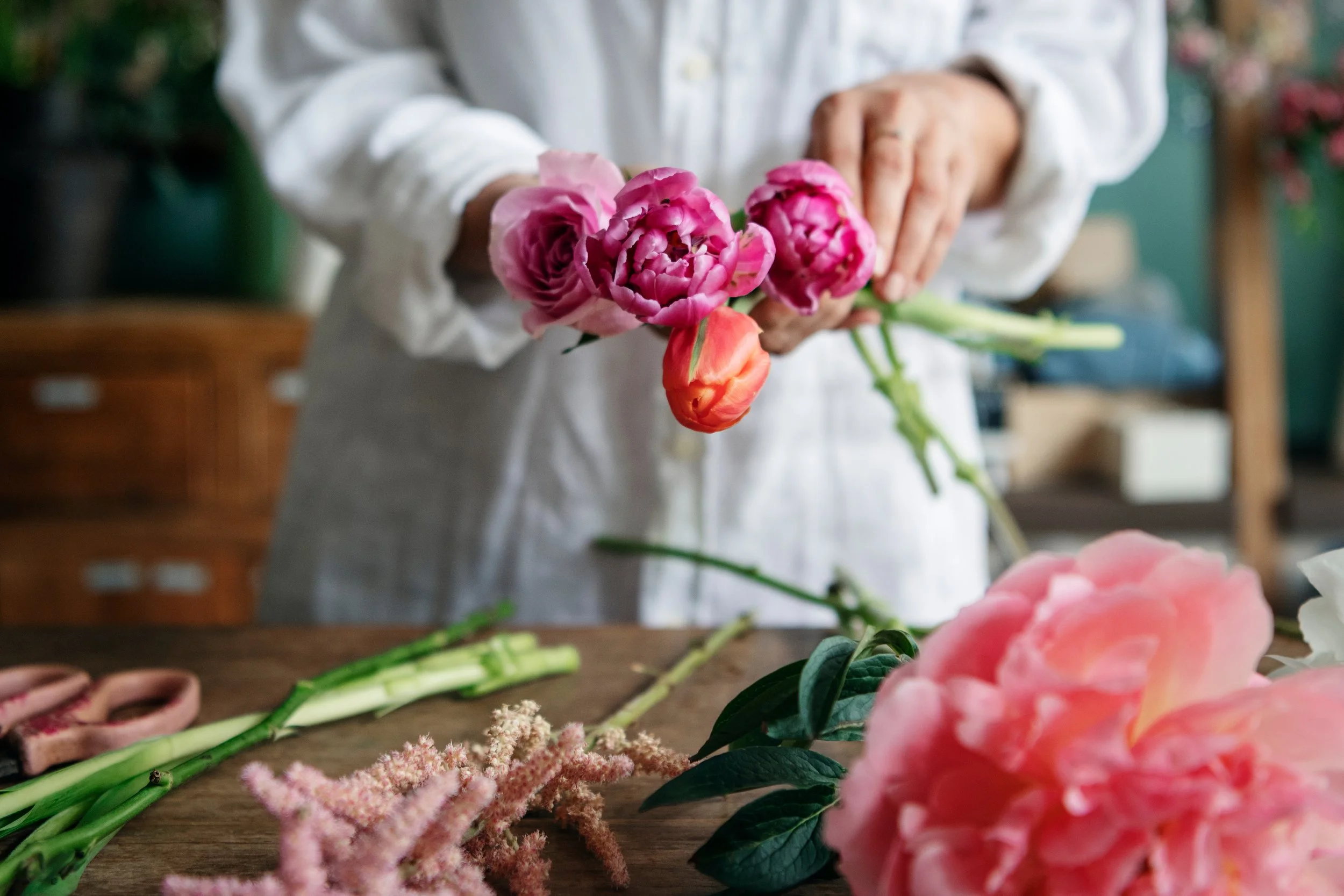 Person arranging pink and orange flowers on a wooden table.