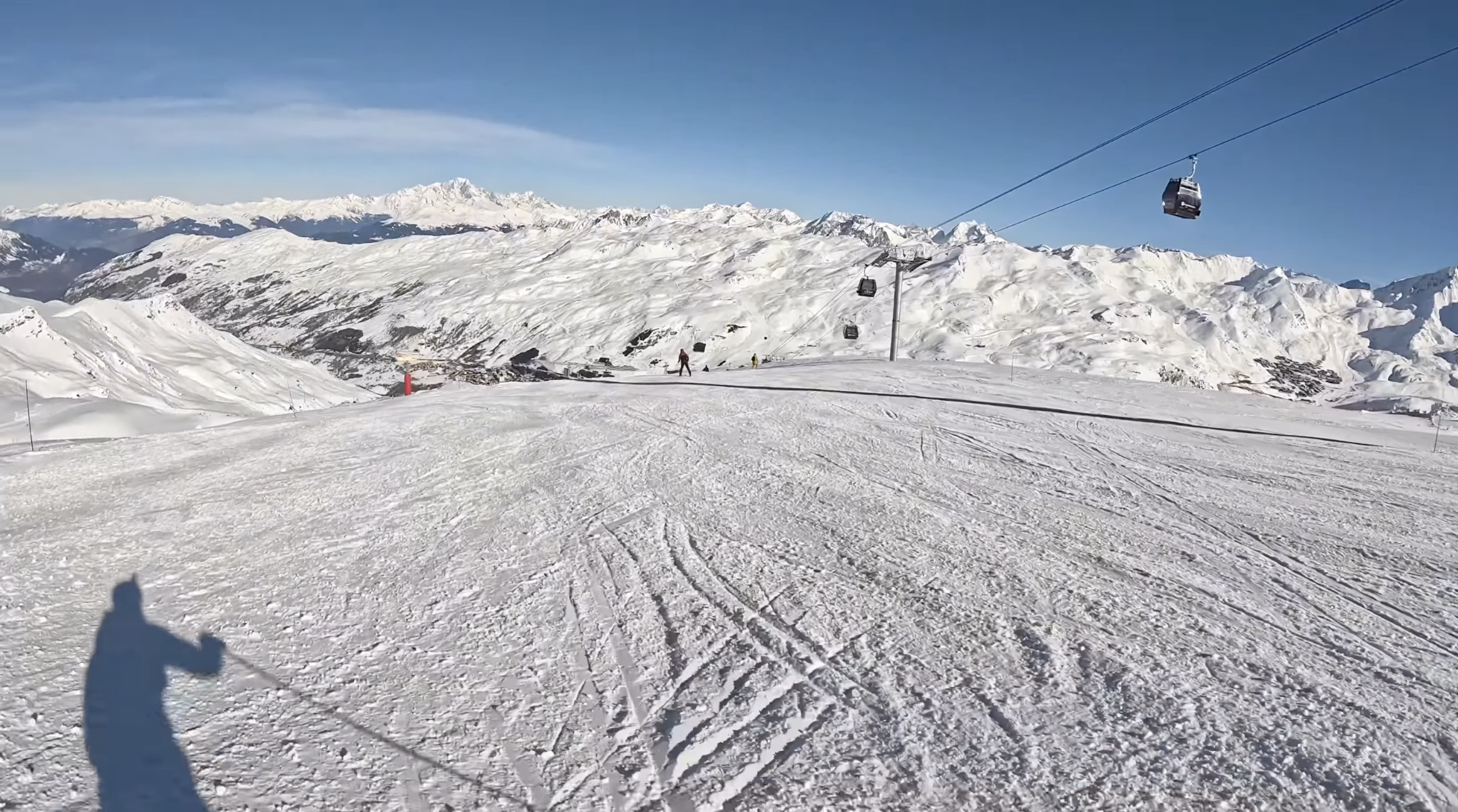 A panoramic view down a ski slope at Les 3 Vallees, France, on a sunny day, with a gondola to the right