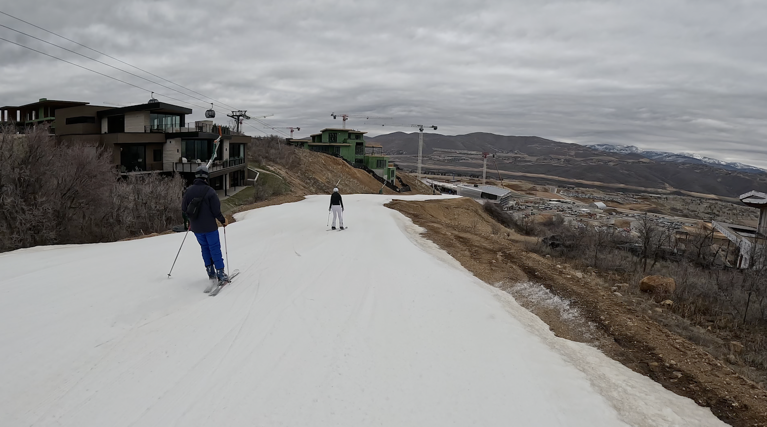 Skiing down a narrow ski trail surrounded by dirt and buildings under construction at Deer Valley ski resort, Utah