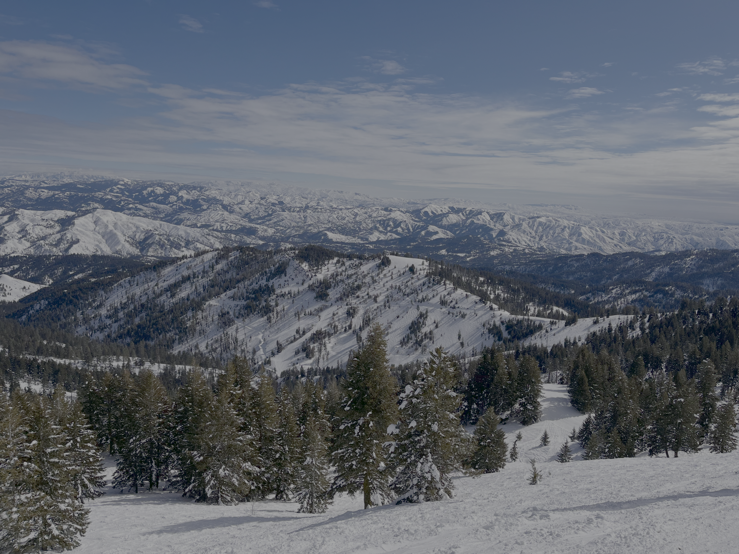 View of snowy mountains and forests from the top of a steep slope at Bogus Basin ski resort, Idaho
