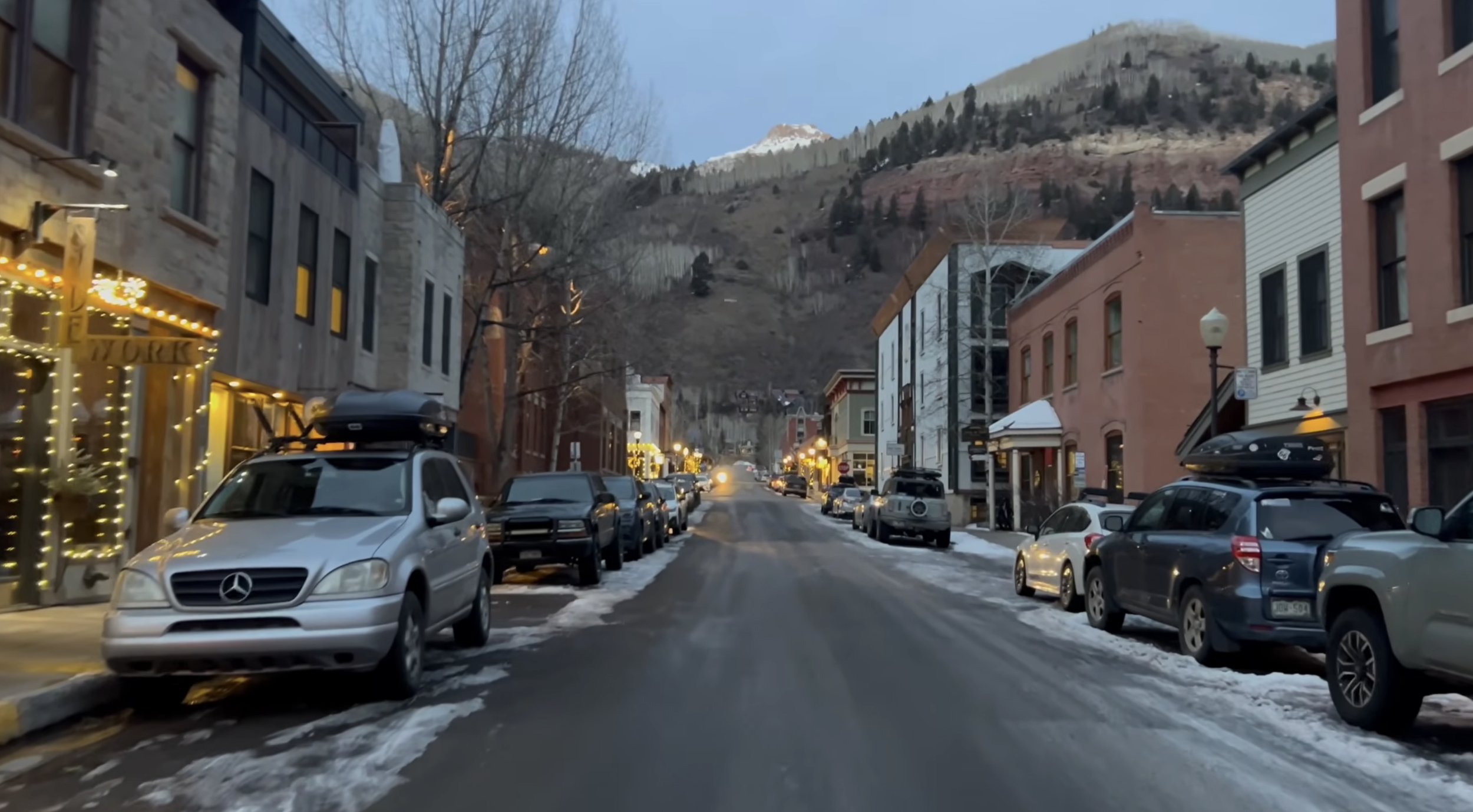 An idyllic city street in Telluride, CO at sunset with cars parked along the sides and red rock hills in the background