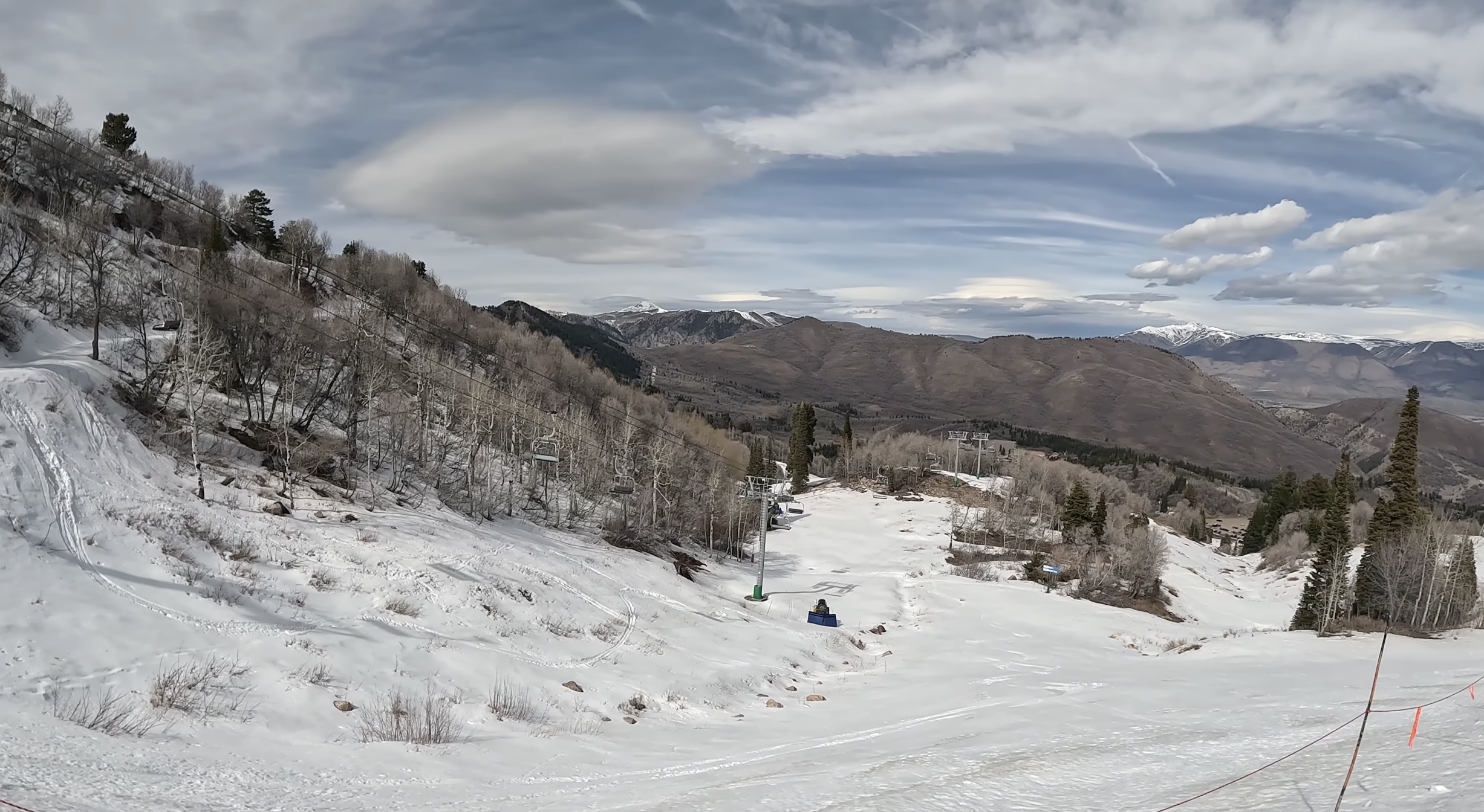 Looking across a wide slope with snow and dirt and a chairlift going up it at Snowbasin ski resort, Utah