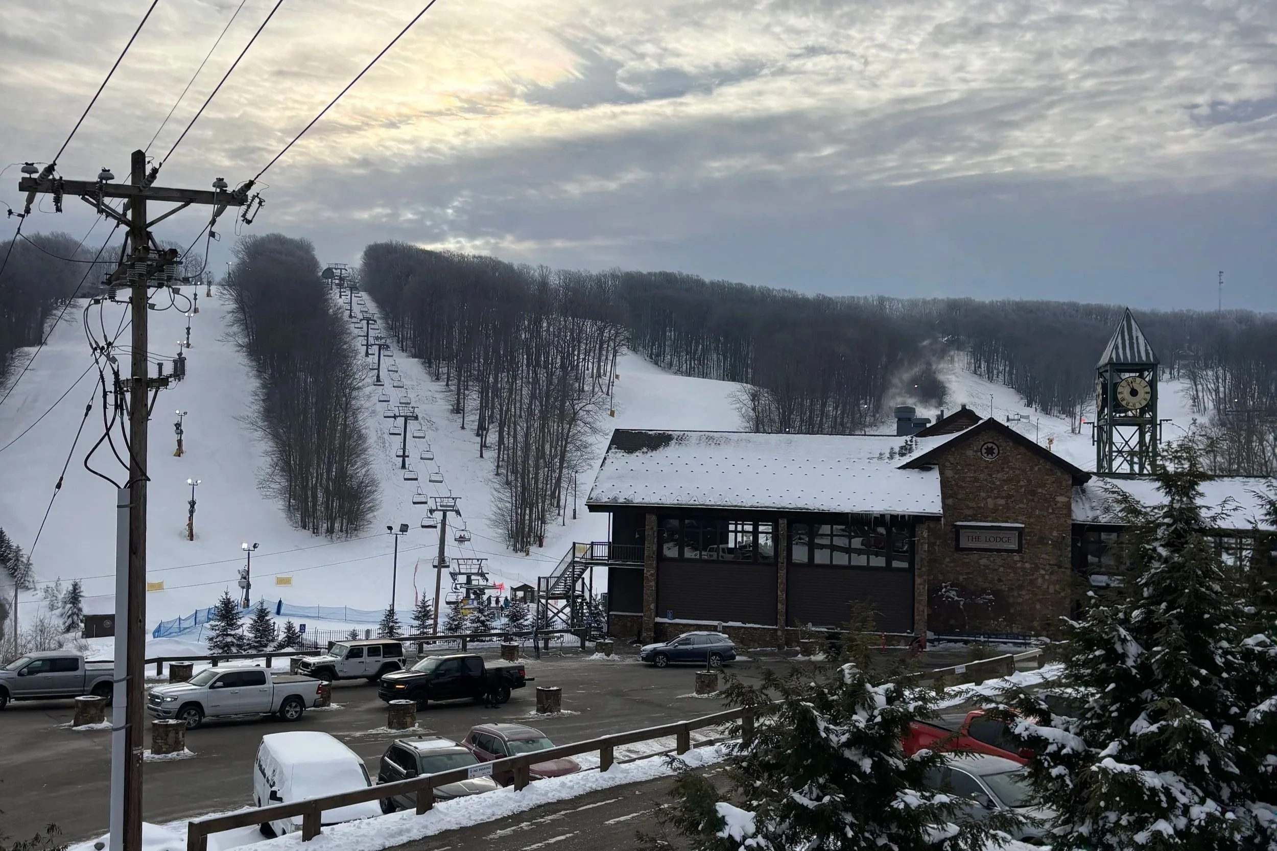 A ski resort base with a clocktower and a chairlift riding up a snowy slope in early morning