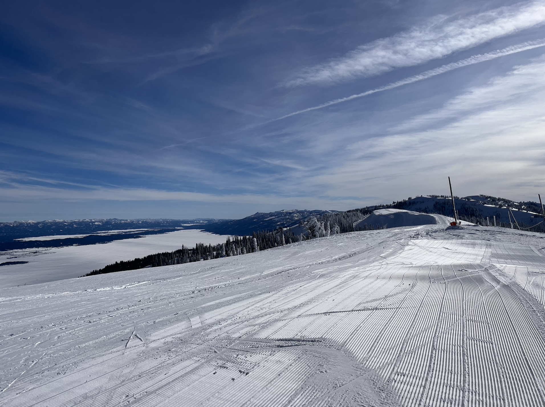 A flat, groomed ski trail with a lake and mountains in the background on a sunny day at Tamarack ski resort, Idaho