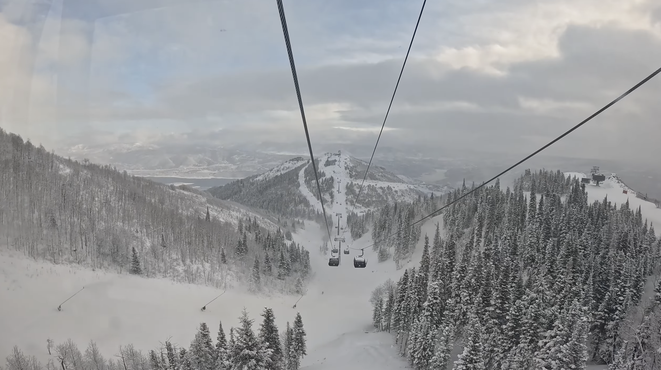 Riding up a gondola on a cloudy day and looking down snowy forested hills at Deer Valley ski resort, Utah