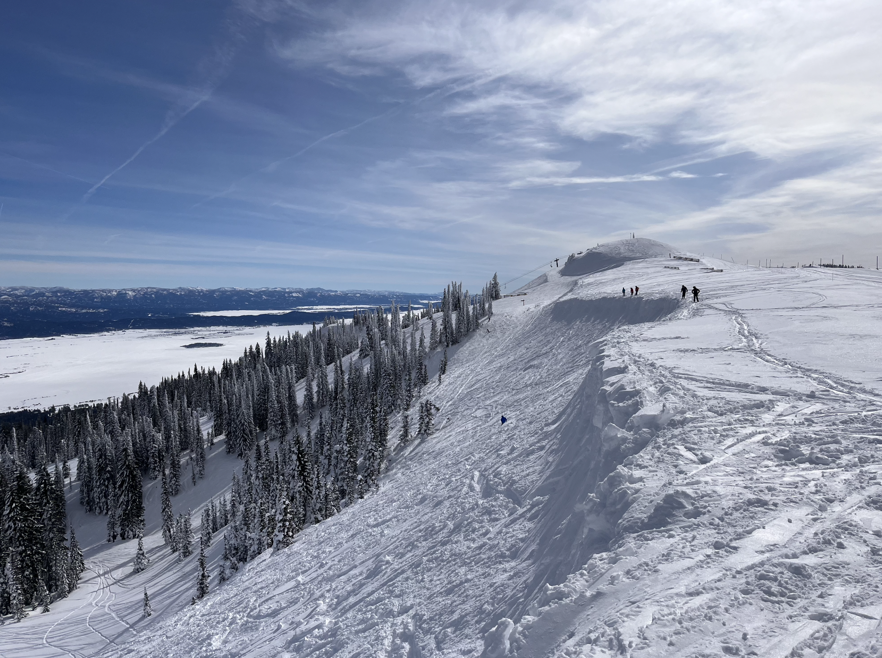 Looking along a steep snowy ridge on a sunny day at Tamarack ski resort, Idaho, with a huge lake in the distance