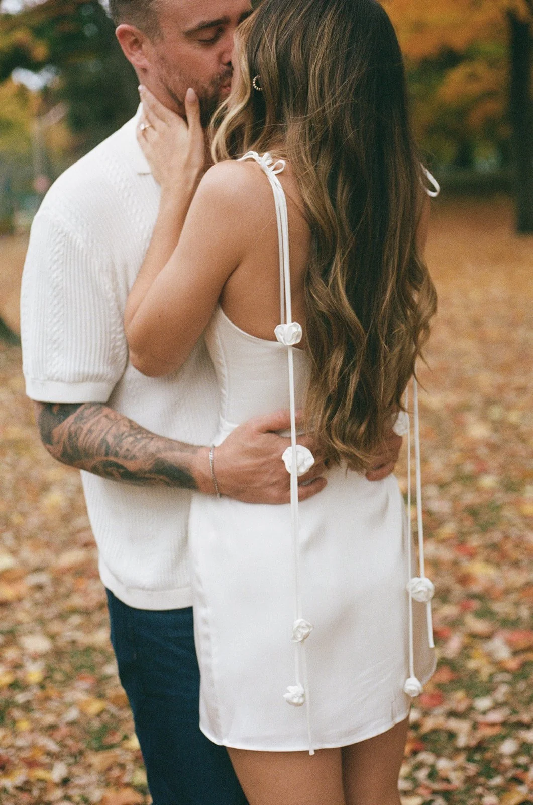 A couple sharing an intimate moment outdoors during fall in High Park, Toronto engagement session, standing close with the woman's hands on the man's face and the man's hands on the woman's waist, surrounded by autumn leaves.