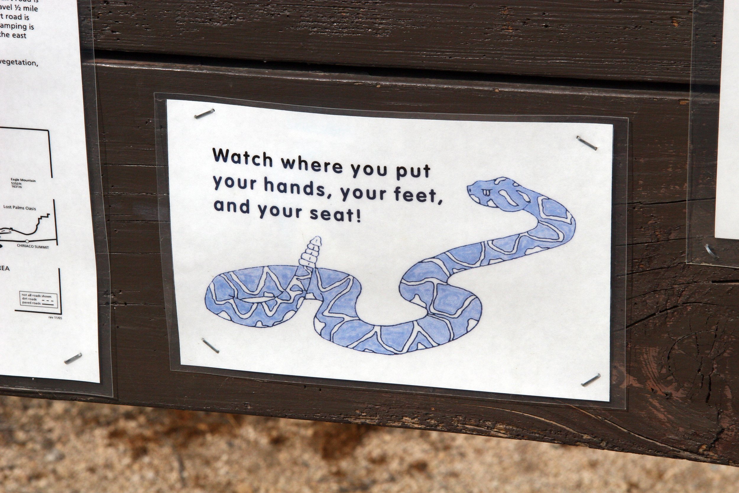 Sign with cartoon illustration of a snake and text that says, "Watch where you put your hands, your feet, and your seat!"