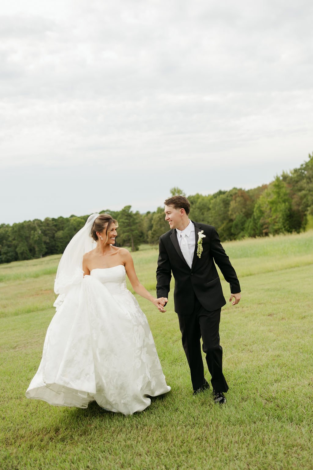 Bride and groom walking through a field on their wedding day in their white dress and black tux