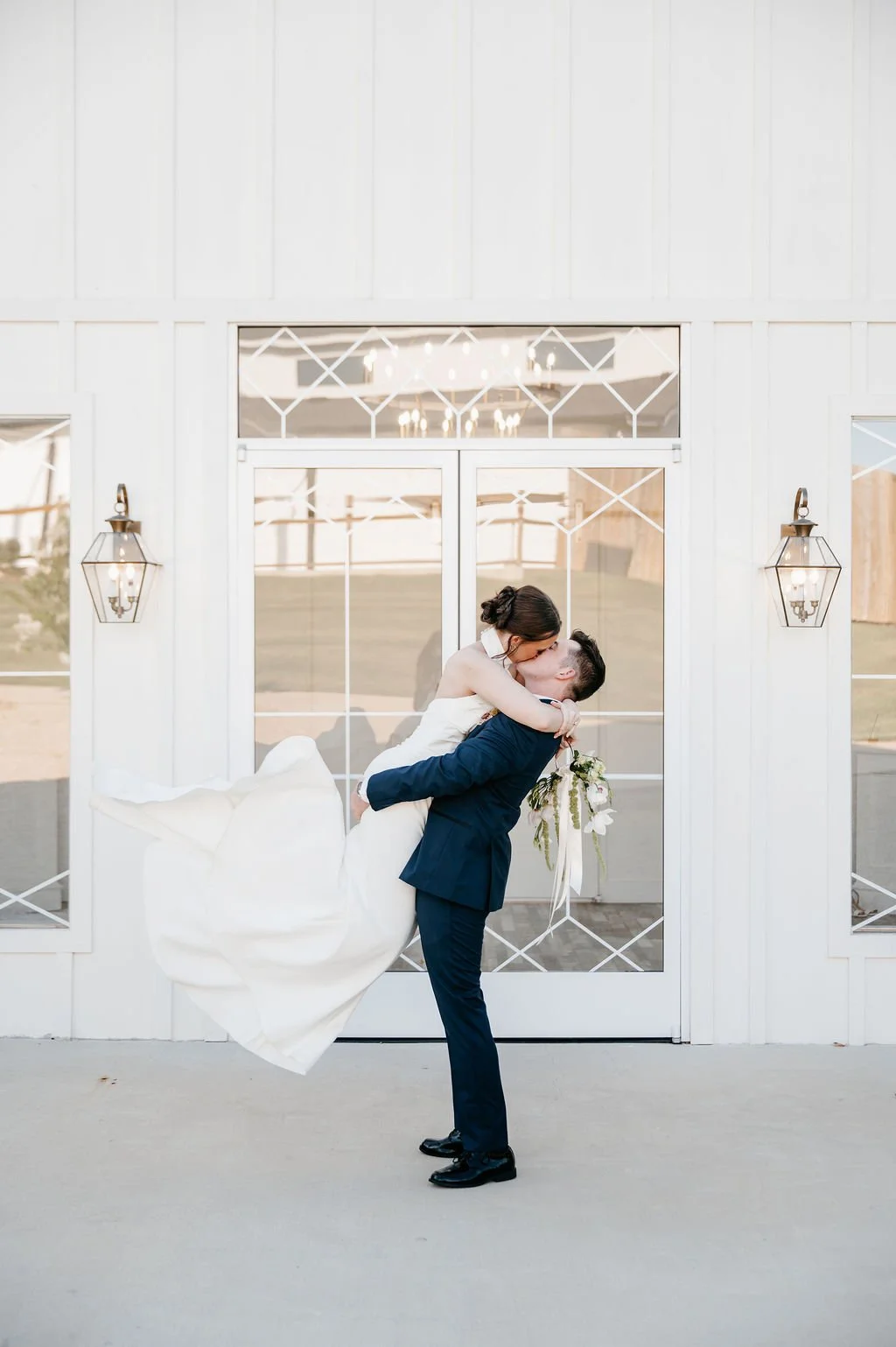 groom in navy suit lifting up his bride and spinning her around in front of east texas elopement chapel
