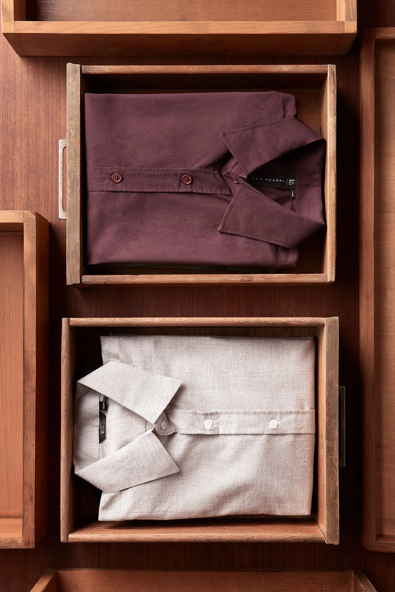 Folded burgundy and beige shirts in wooden boxes on a wooden surface. Fashion flatlay photography Los Angeles.