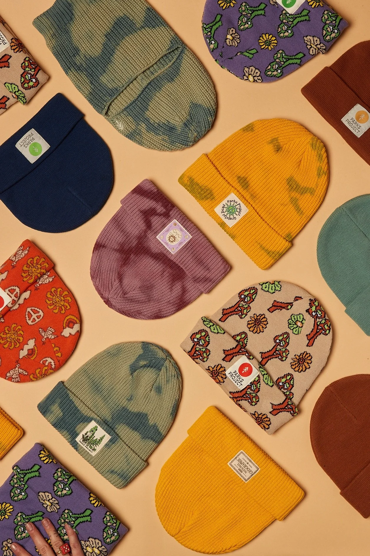 Arrangement of colorful knit beanies and socks on a beige background, with various patterns including camouflage, floral, animal, and abstract designs. Fashion flatlay photography Los Angeles.