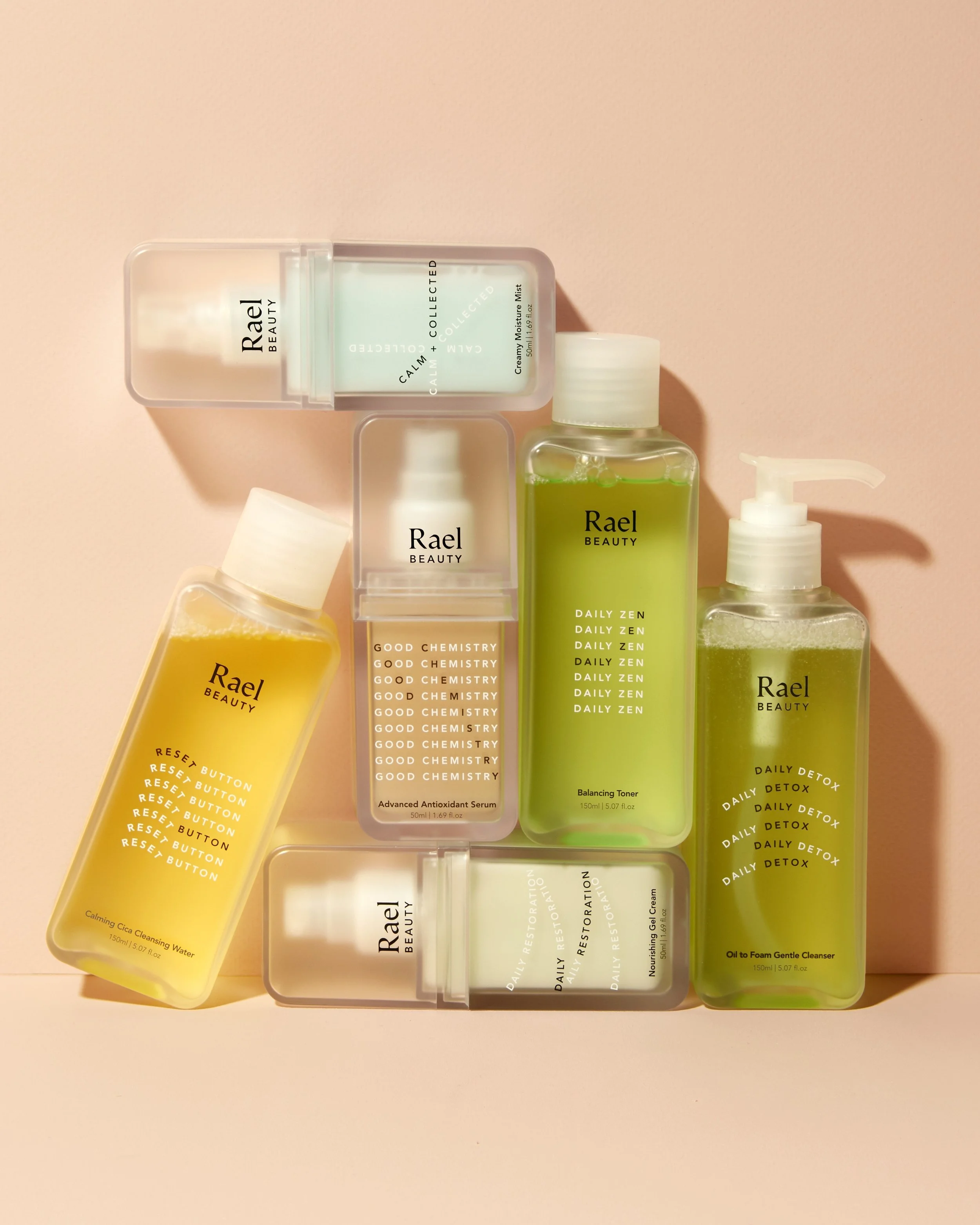 Collection of skincare bottles from Rael Beauty with green, yellow, and clear liquids on a pink background. Beaty Photography Los Angeles.
