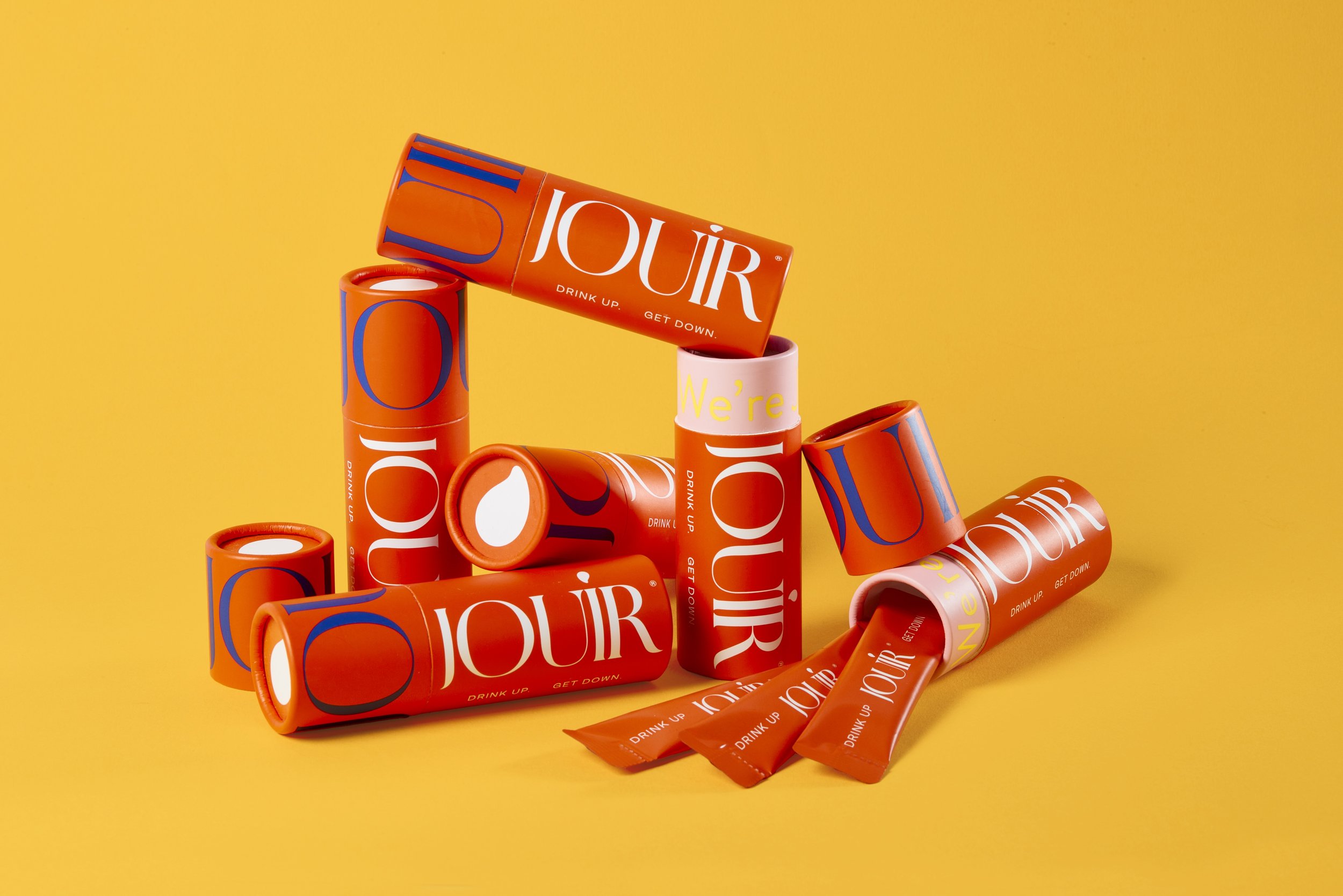 Multiple orange and pink Jouir cans on a yellow background. Beaty Photography Los Angeles.