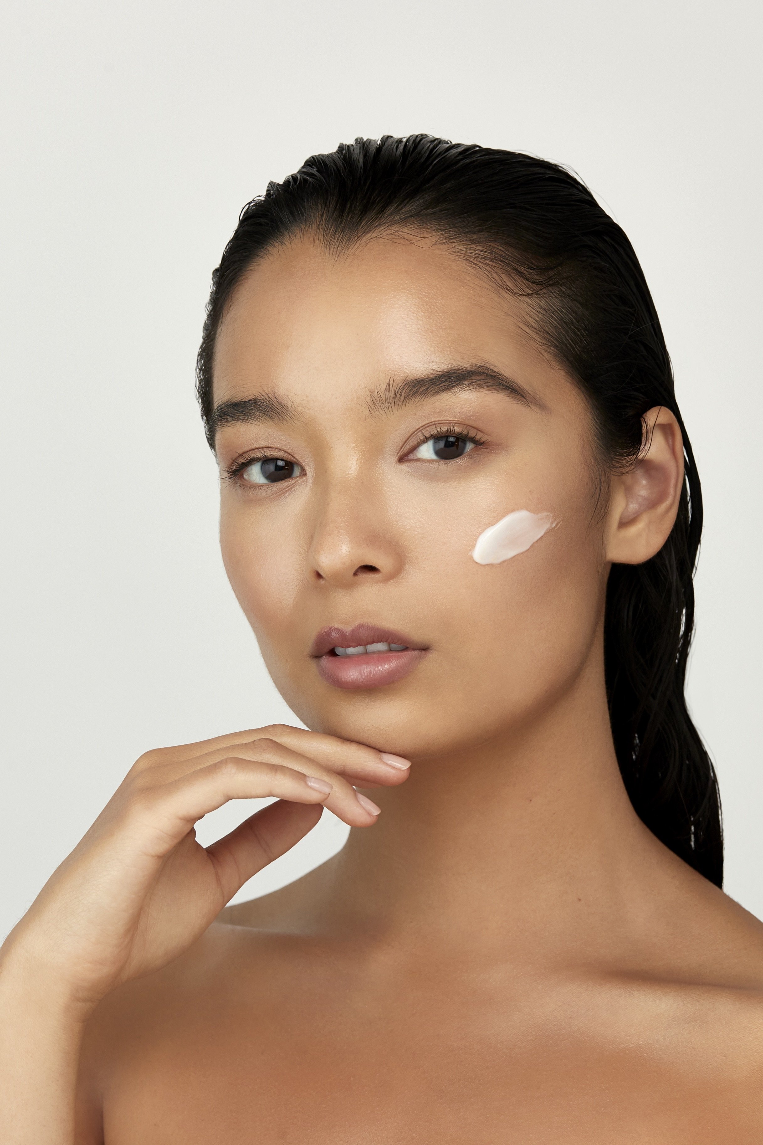 A woman with dark hair pulled back, applying moisturizer or sunscreen to her face. Beaty Product Photography Los Angeles.