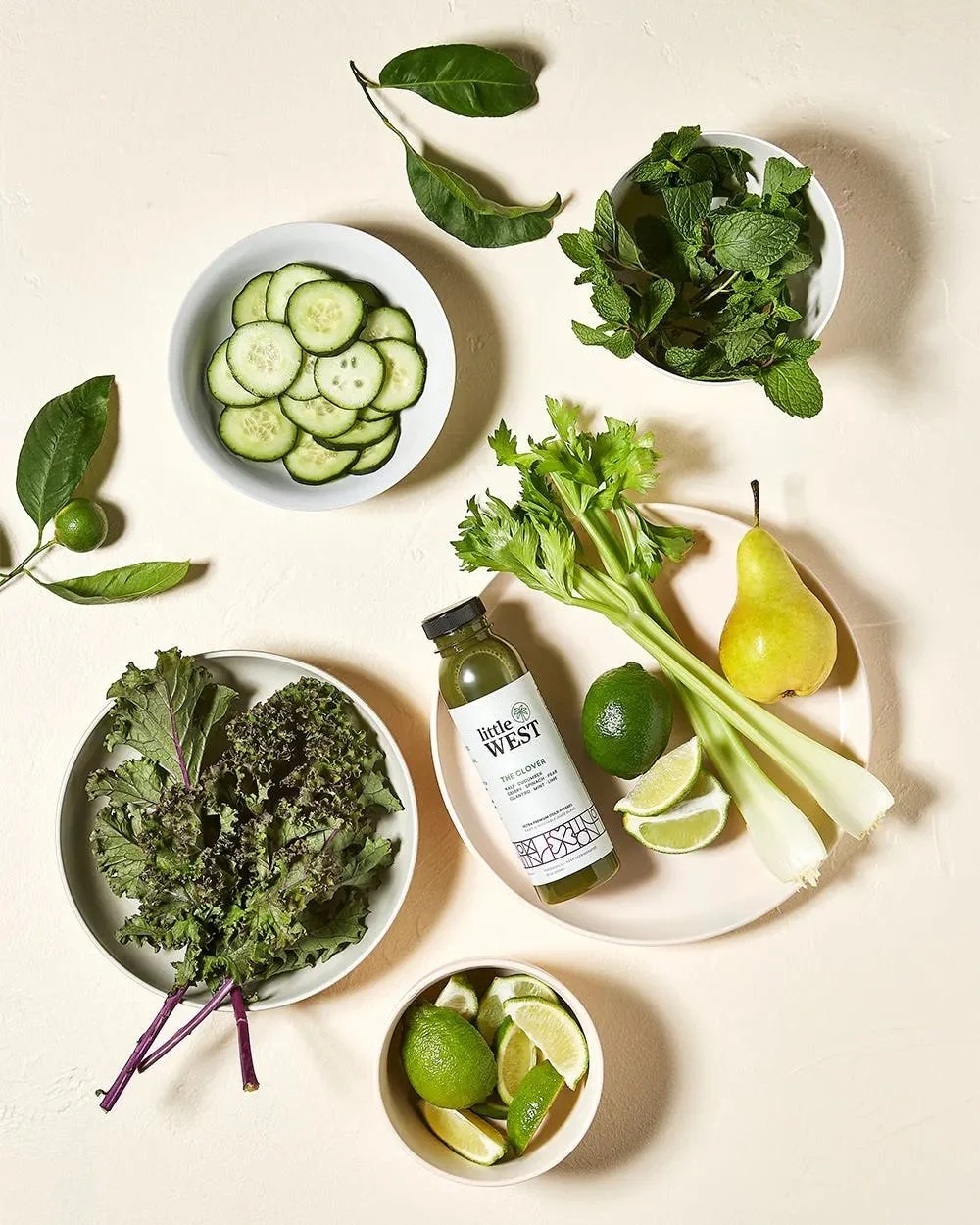 Cucumbers, mint, celery, lime wedges, lemon, green apple ingredients shot with a greendrink by Little West. Los Angeles beverage and food photography.