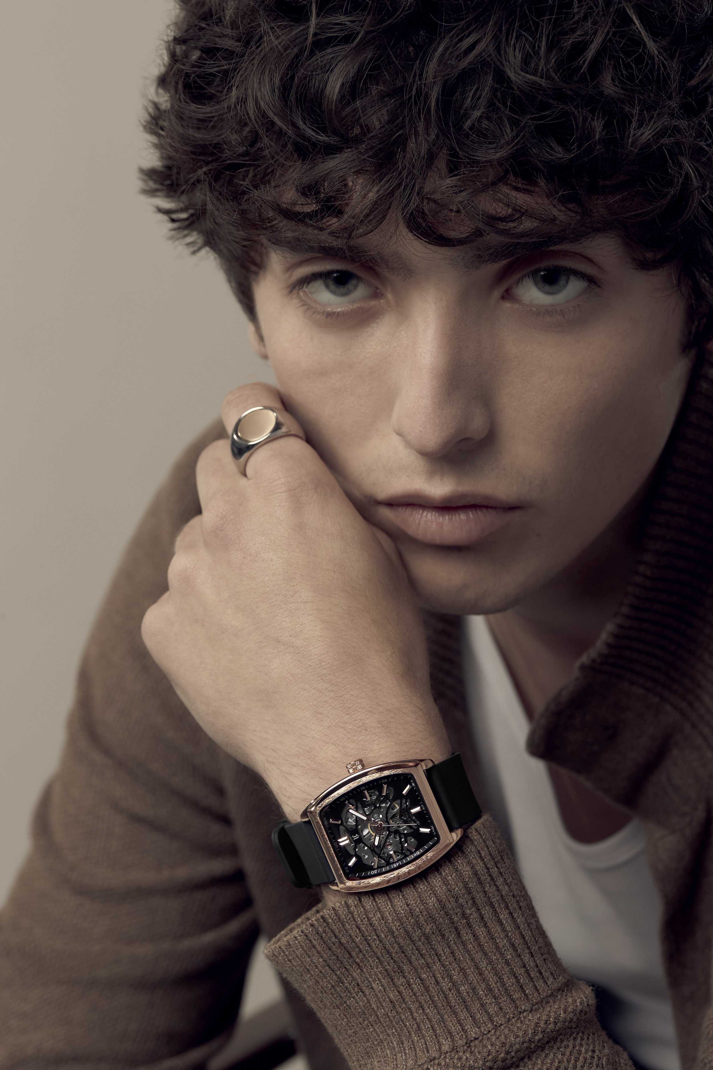 Close-up of a young man with curly hair wearing a watch on his wrist and a ring on his finger, looking intently at the camera. On model fashion photography, Los Angeles.