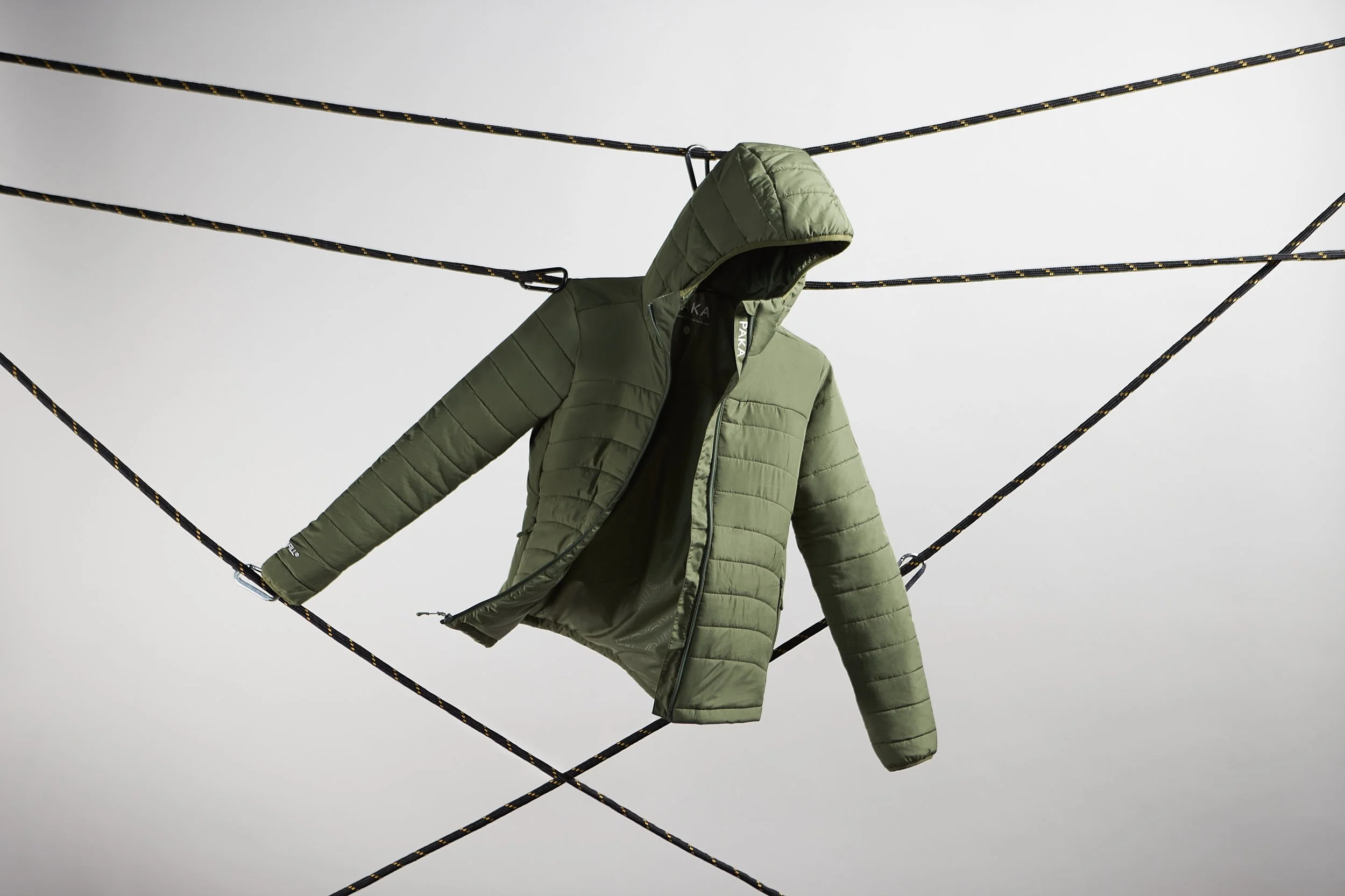 Green puffer jacket hanging on a clothesline against a cloudy sky. Product photography Los Angeles.
