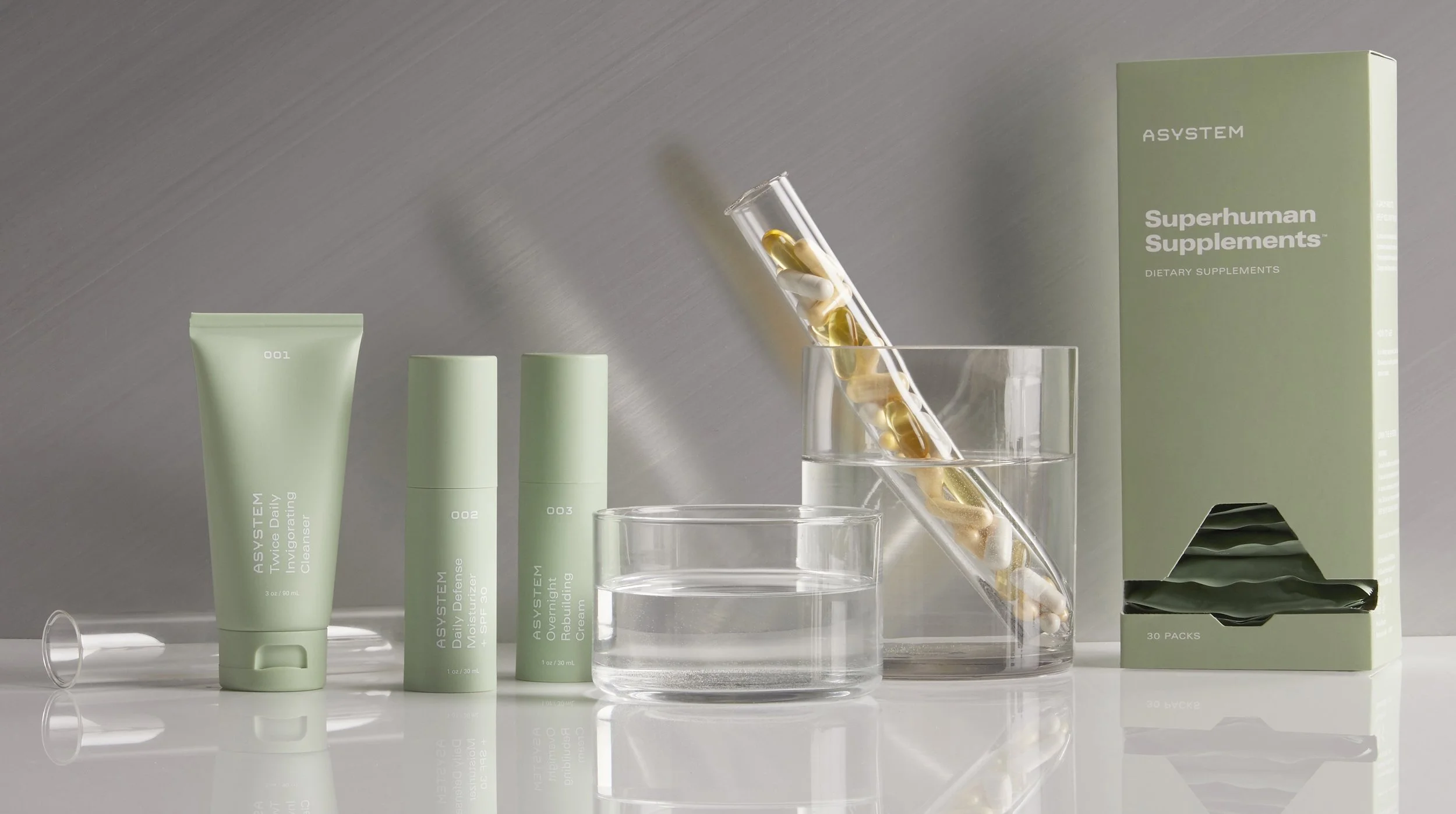 A collection of skincare products and supplements on a white surface, including a tube and bottles labeled "AYSTEM" and "Superhuman Supplements," with pills in a test tube and water. Los Angeles beauty product photography.