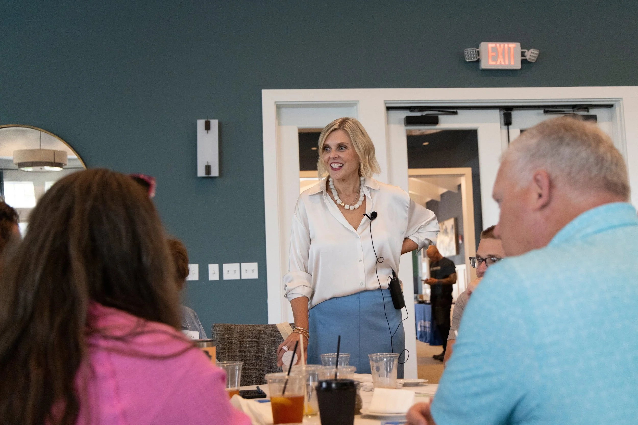 Krista Demcher standing and talking with attendees seated at tables during a workshop