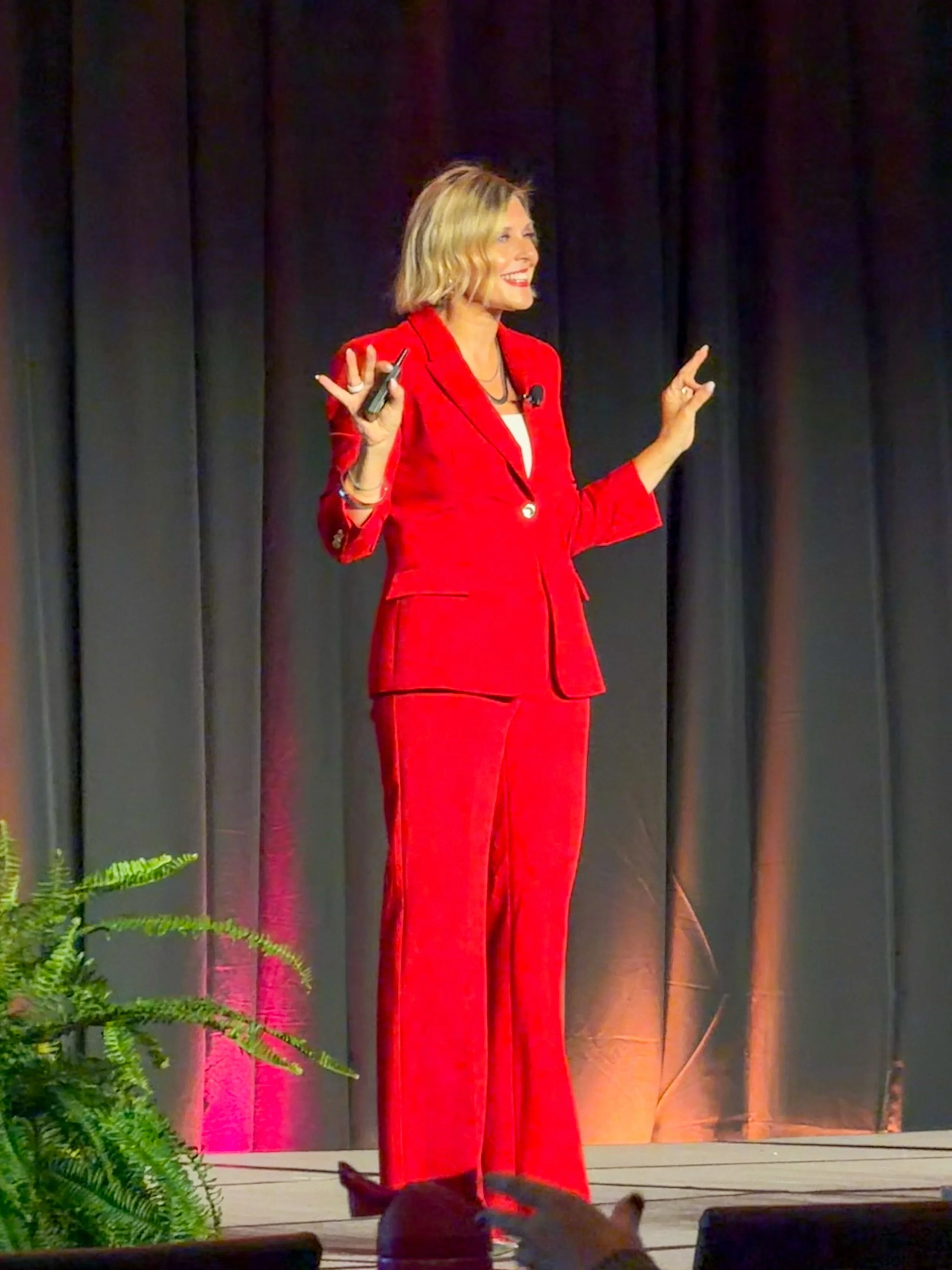 Krista Demcher in a red pantsuit presenting on a dark stage at the Elevate Conference in Nashville