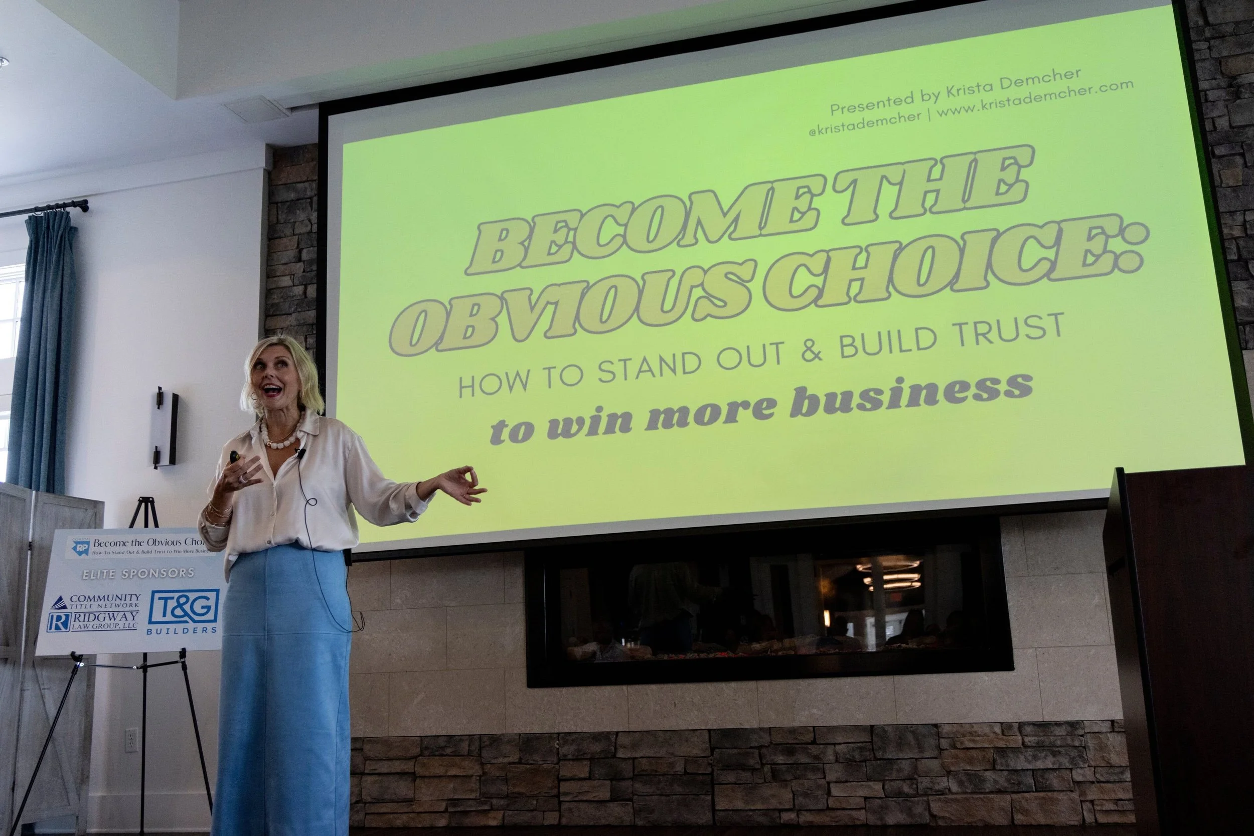 Krista Demcher gesturing as she speaks in front of a large screen reading Become the Obvious Choice: How to stand out and build trust to win more business