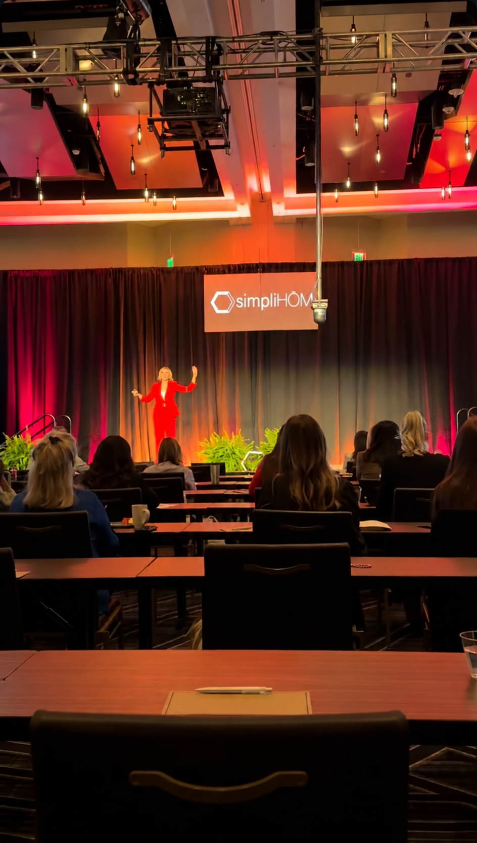 Krista Demcher in a red pantsuit presenting on a dark stage at the Elevate Conference in Nashville