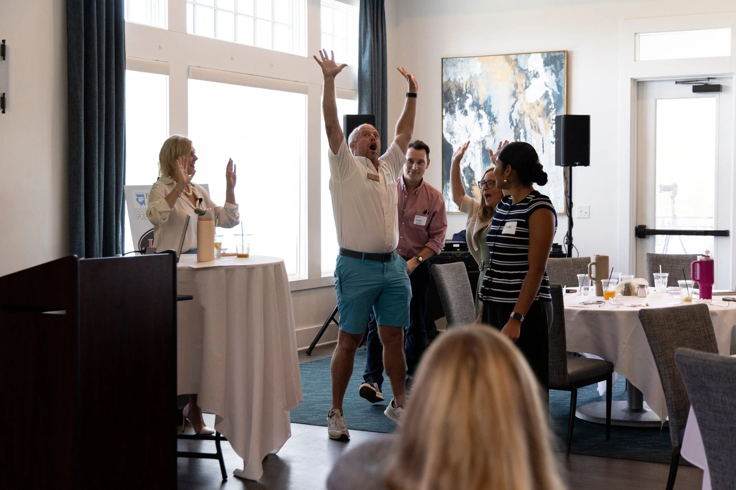 Krista Demcher leading a group exercise with one audience participant with his hand up in the air