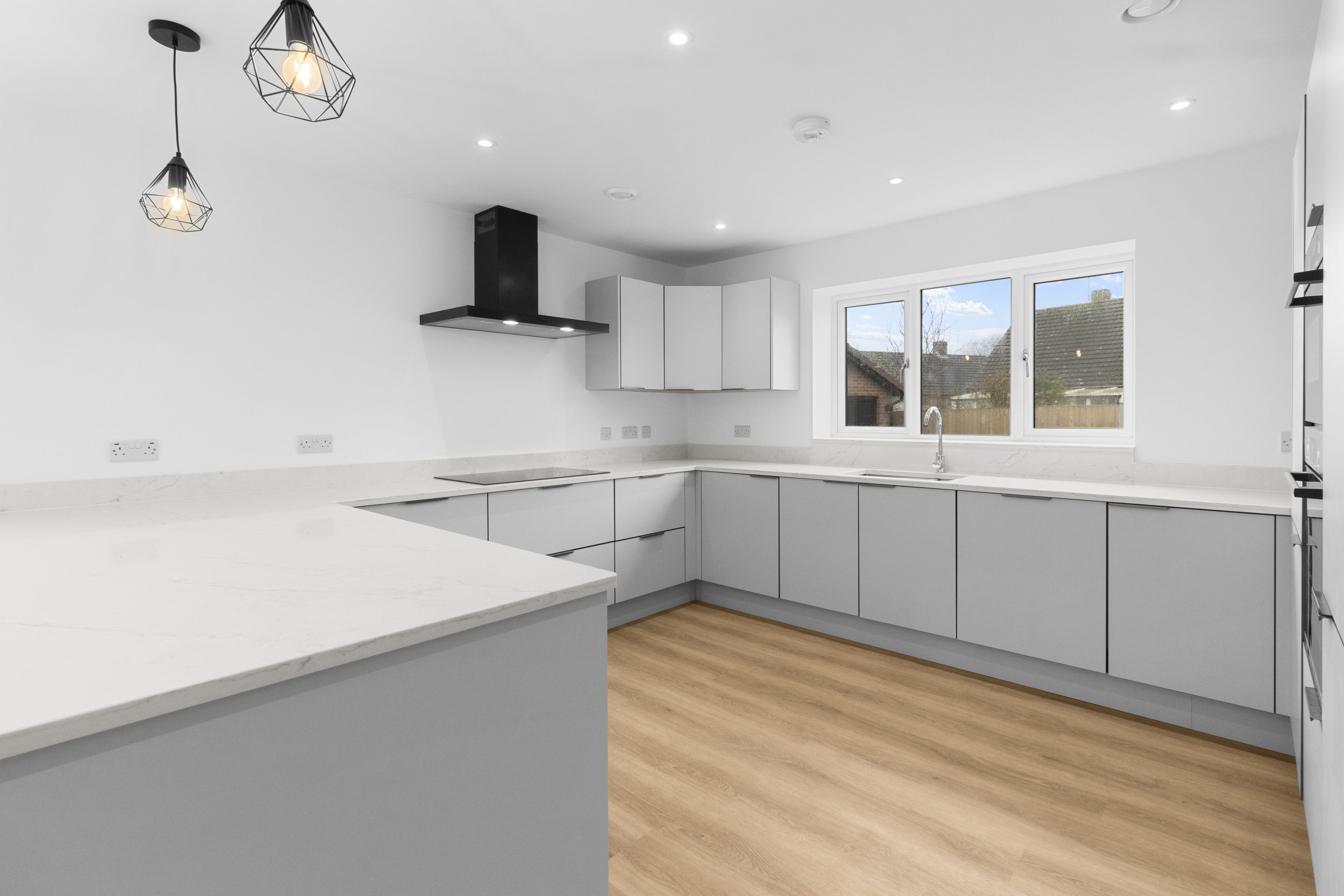Modern kitchen with white cabinets, marble countertops, black range hood, pendant lights, wood flooring, and a window view.