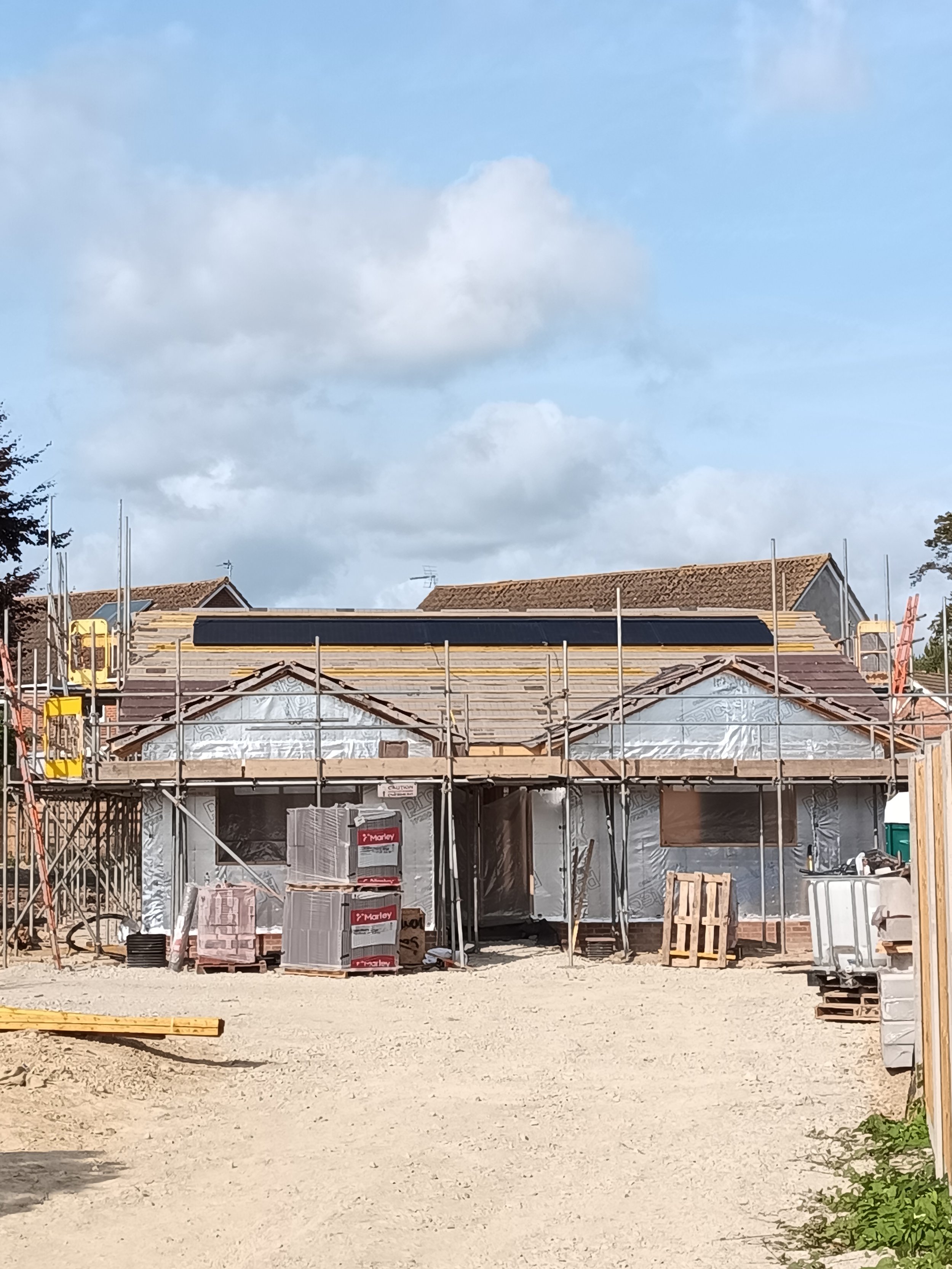 A house under construction surrounded by scaffolding, building materials, and a clear sky above.