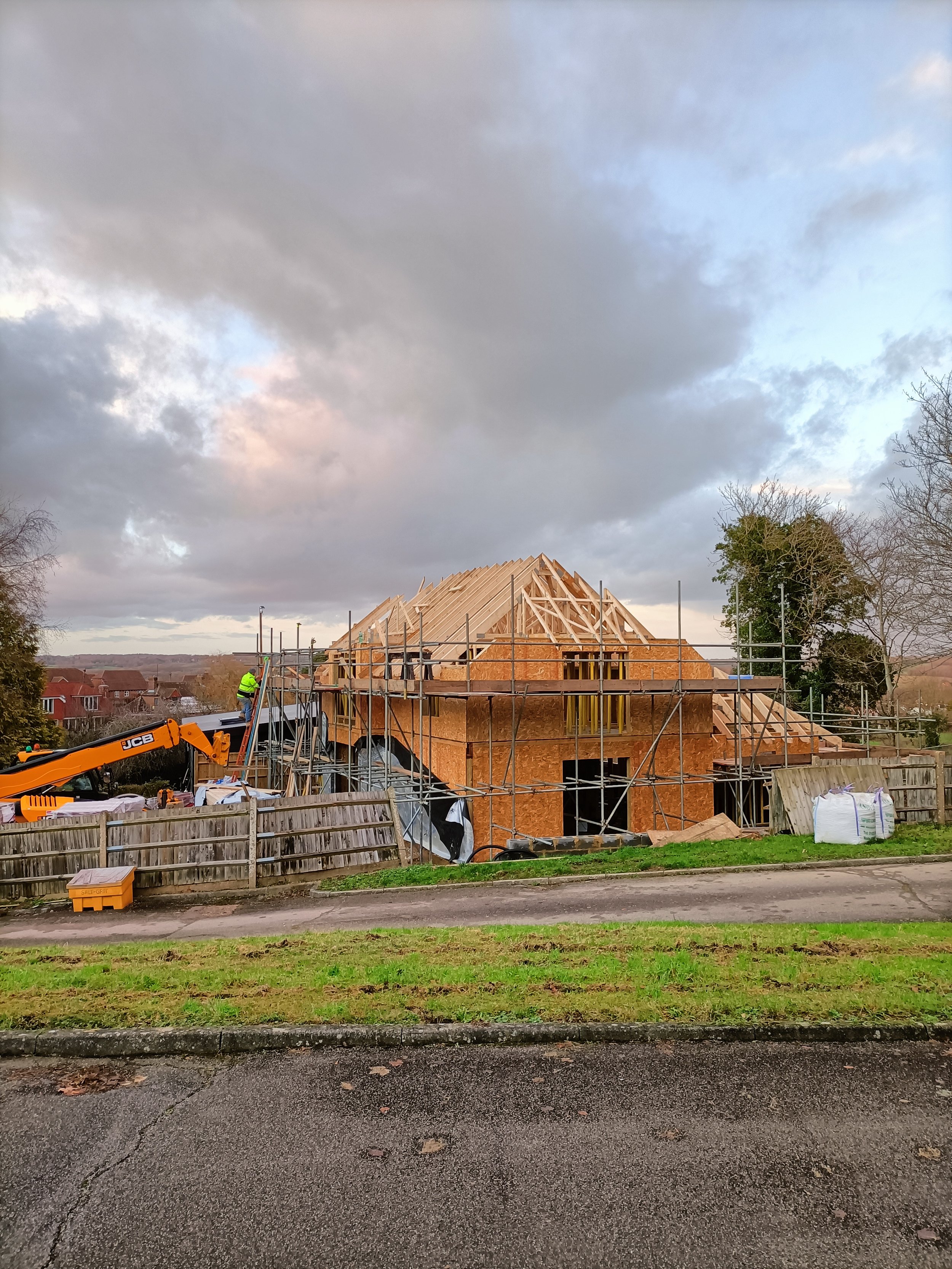 House under construction with scaffolding, wooden framing, and a crane on site