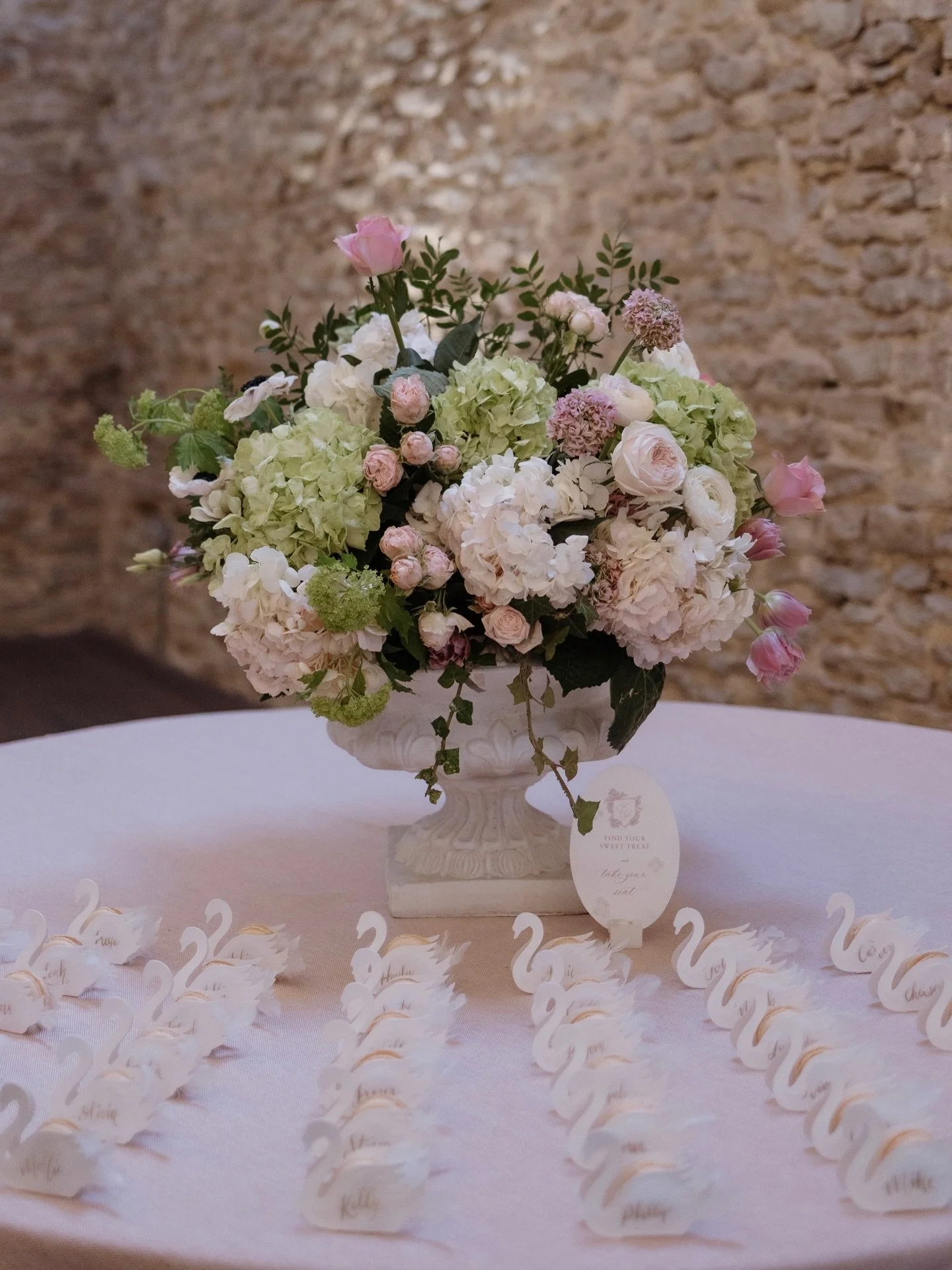 A swan-filled escort table moment at Holesfoot. Delicate, romantic, and just a little bit magical. Textured card swans layered with soft vellum and gold calligraphy names, each finished with a cloud of white feathers and a sweet macaron to welcome gu