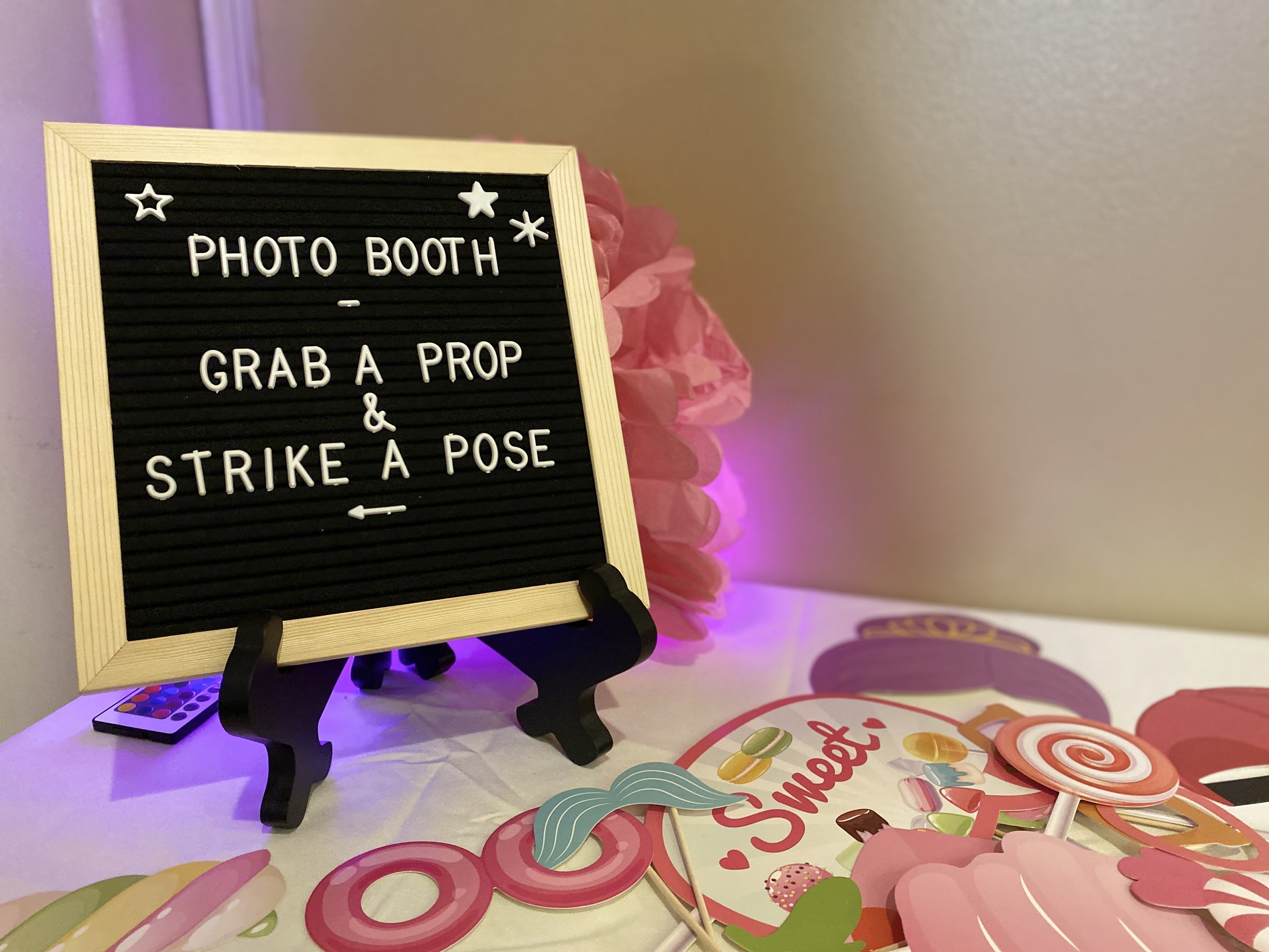 Photo booth setup with a sign reading 'Photo Booth - Grab a Prop & Strike a Pose' surrounded by colorful props including lollipops and sweets.