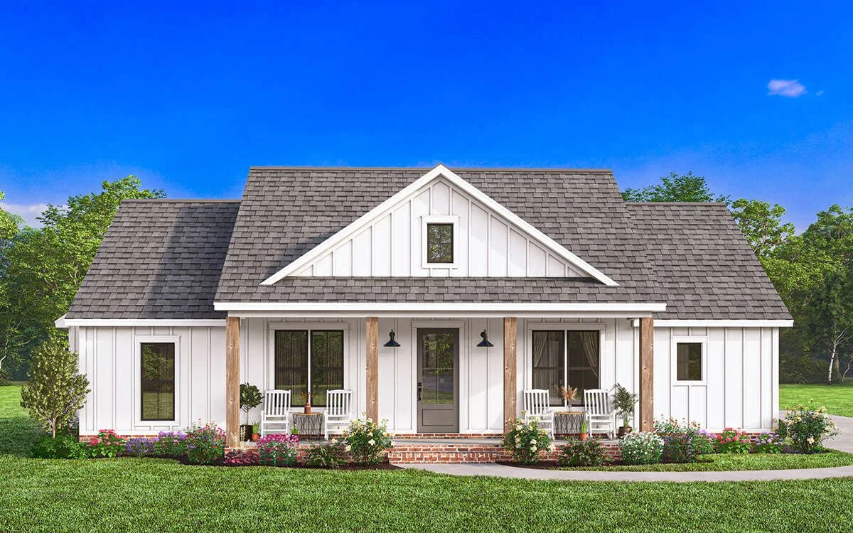 White farmhouse-style home with a gray shingle roof, front porch with two wooden columns, and outdoor seating. Surrounded by greenery and blooming flowers.