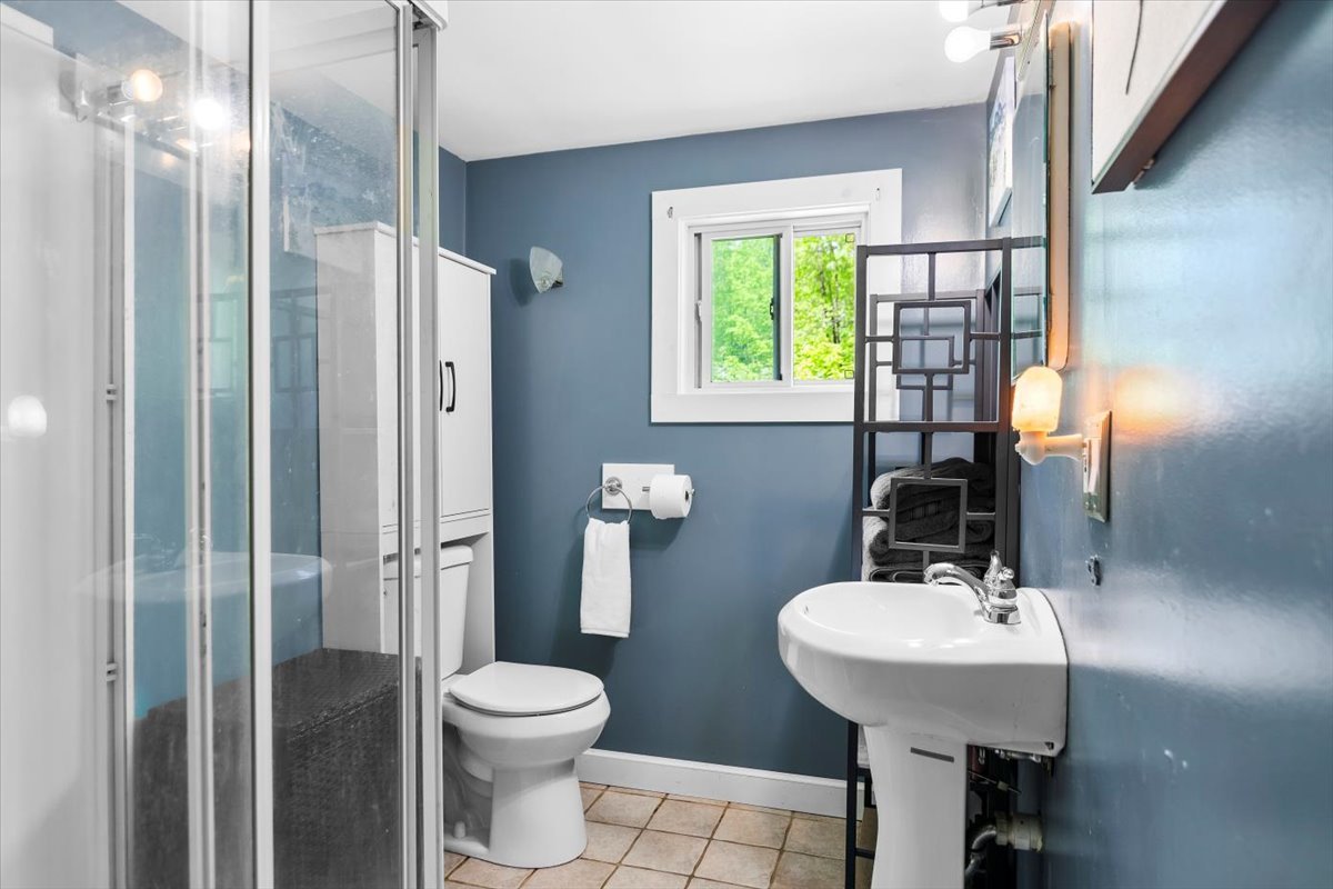 Blue bathroom with pedestal sink, shelving, shower, storage and window in house for sale in Shaftsbury, VT.
