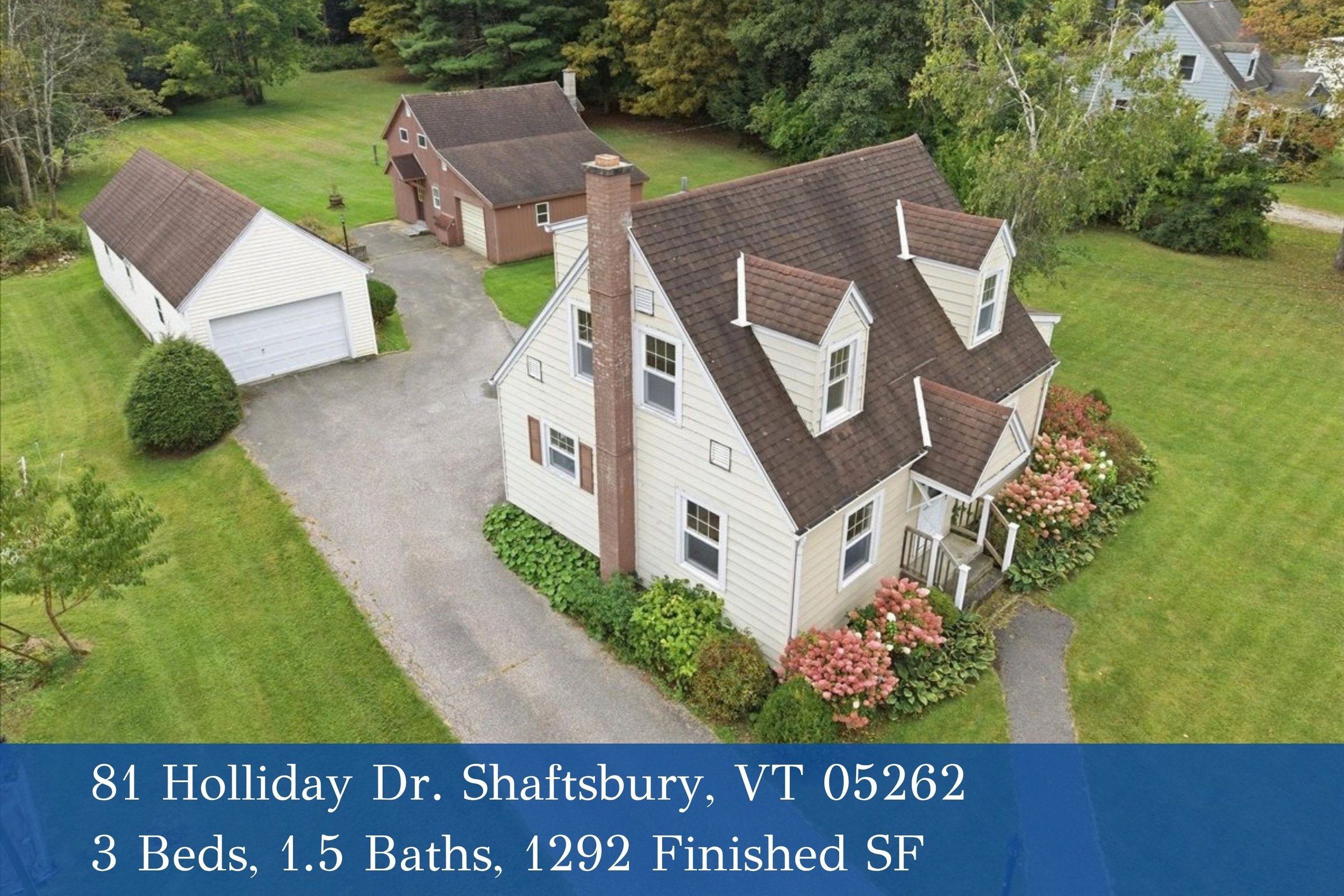 Aerial view of a house with a front porch, surrounded by green lawn and trees, with a detached garage in the driveway, in Shaftsbury, Vermont.